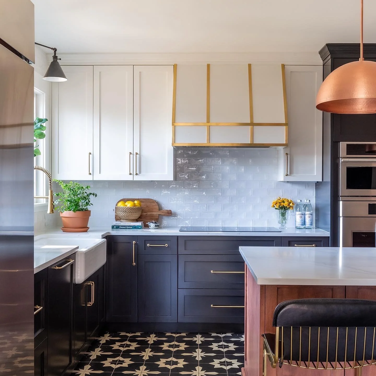 Modern kitchen with black and white cabinets, white subway tile backsplash, and gold accents. Includes potted plants, yellow lemons, glass bottles, and black and white patterned floor. Heartwood Renovations. West Hartford, CT