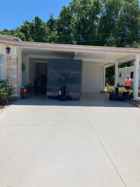 Garage with portable electric scooter, person on the right, and potted plants, trees in background.