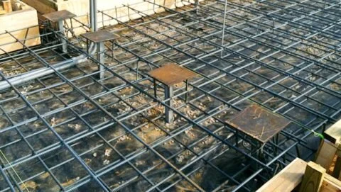 Steel rebar grid on concrete foundation with wooden formwork and some rusted metal supports