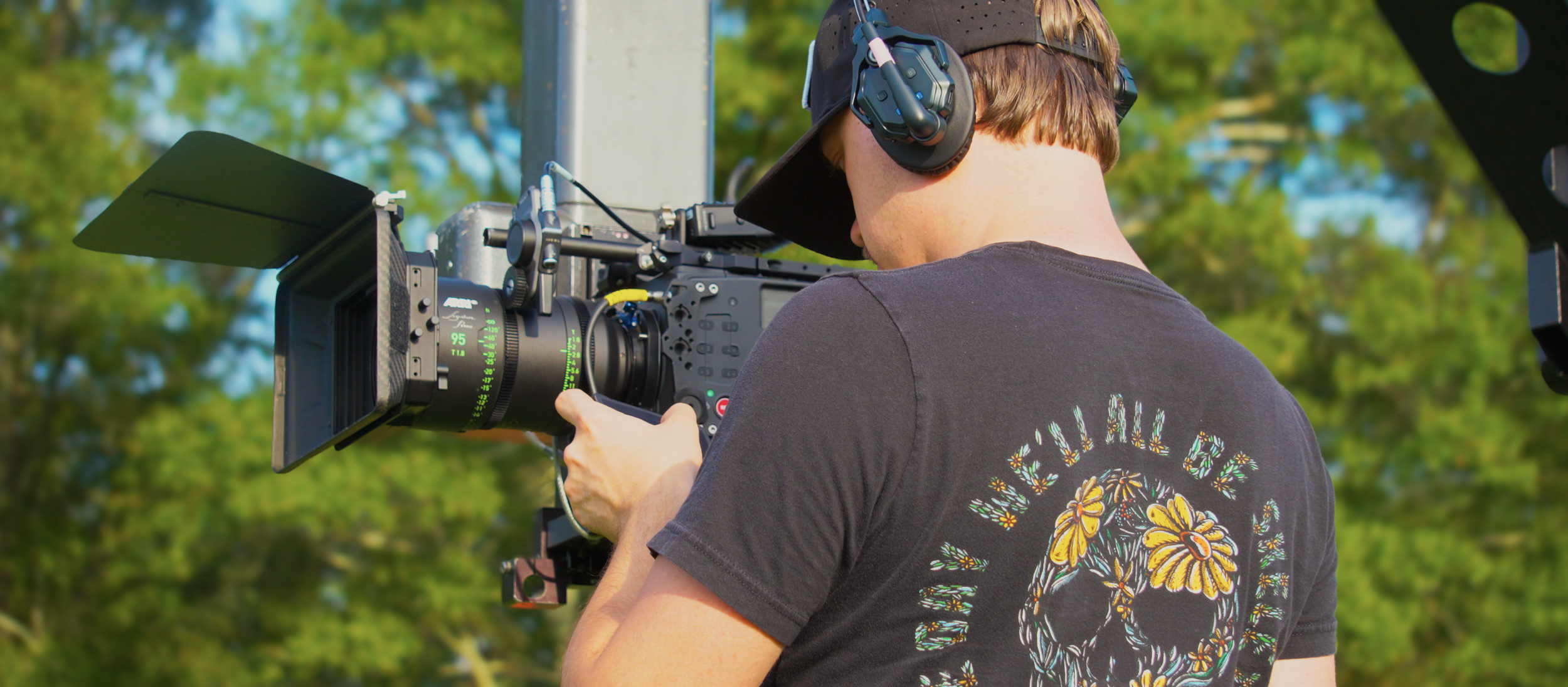 A person operating a professional video camera outdoors during daytime.