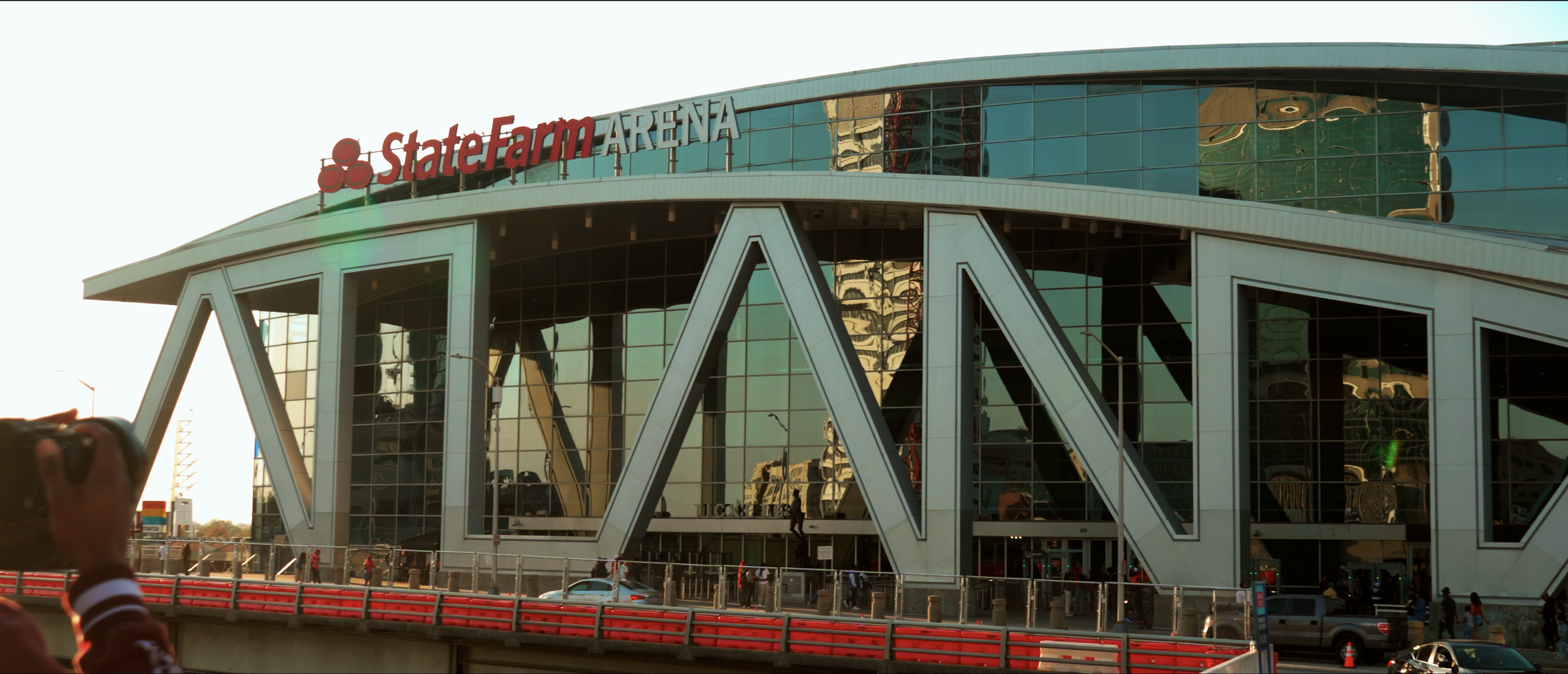 The exterior of State Farm Arena, a modern building with glass walls and large structural beams, with a sign reading 'State Farm Arena' at the top.