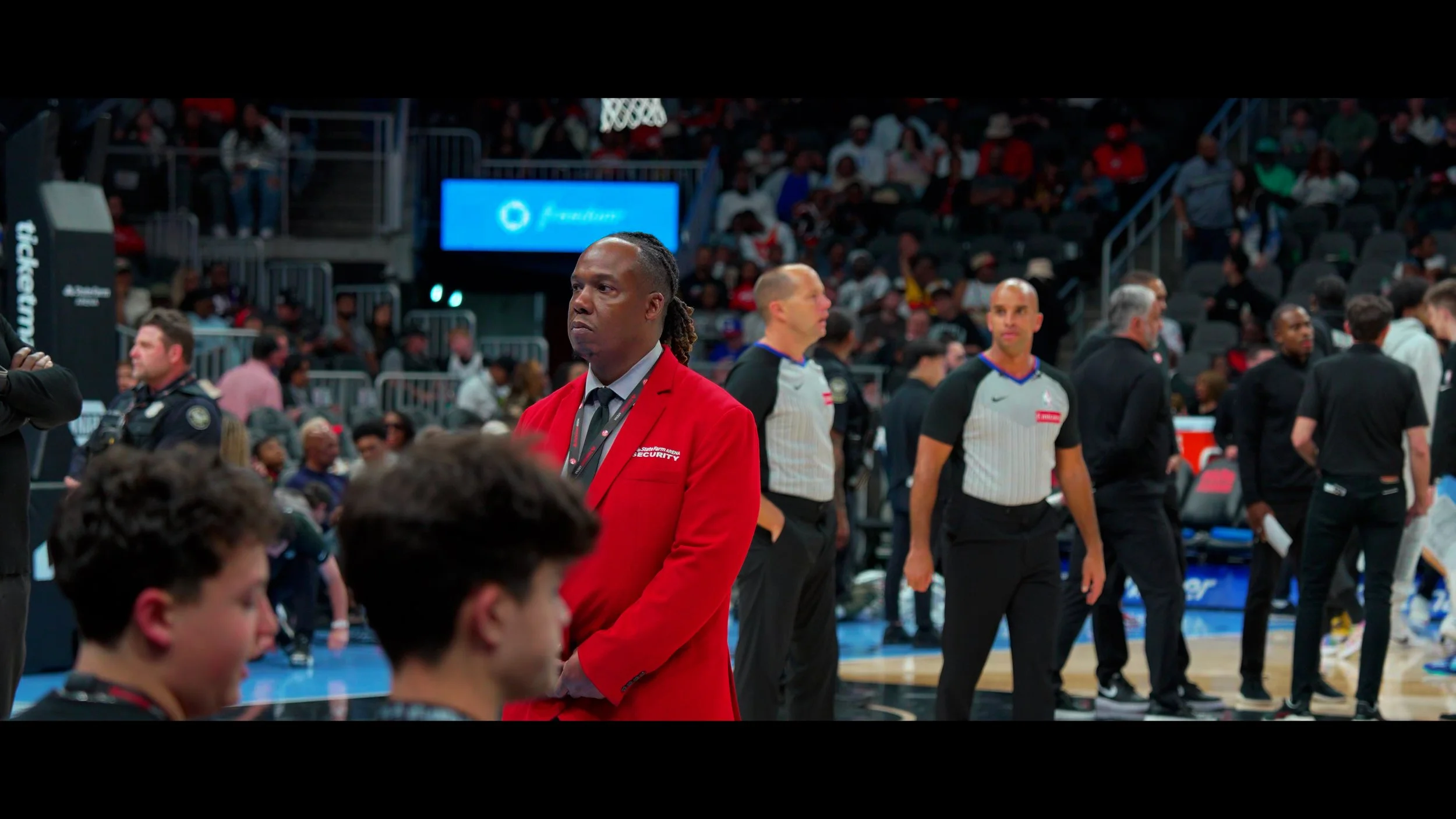 Security personnel and referees at a basketball game, with spectators in the background.