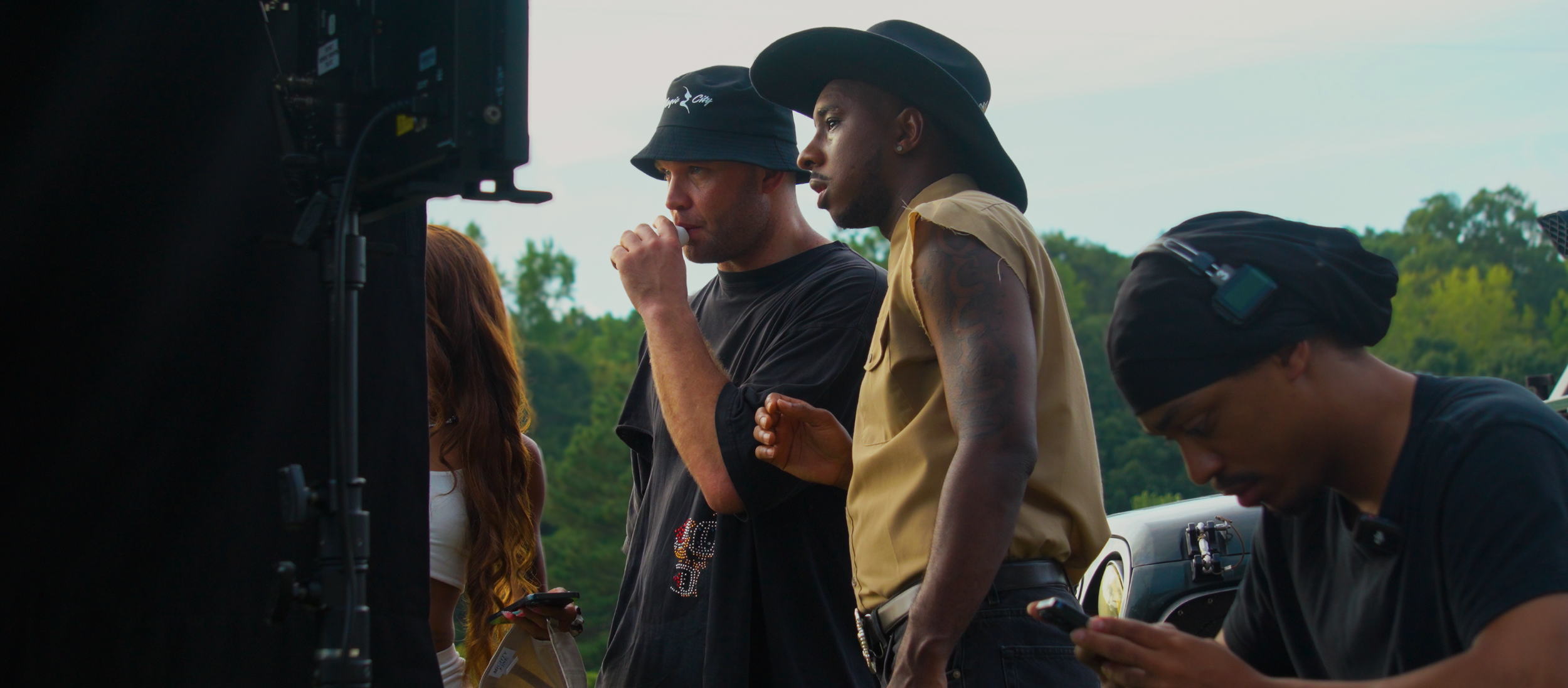 Filmmakers and crew members working on a set outdoors, some wearing hats and using mobile devices.