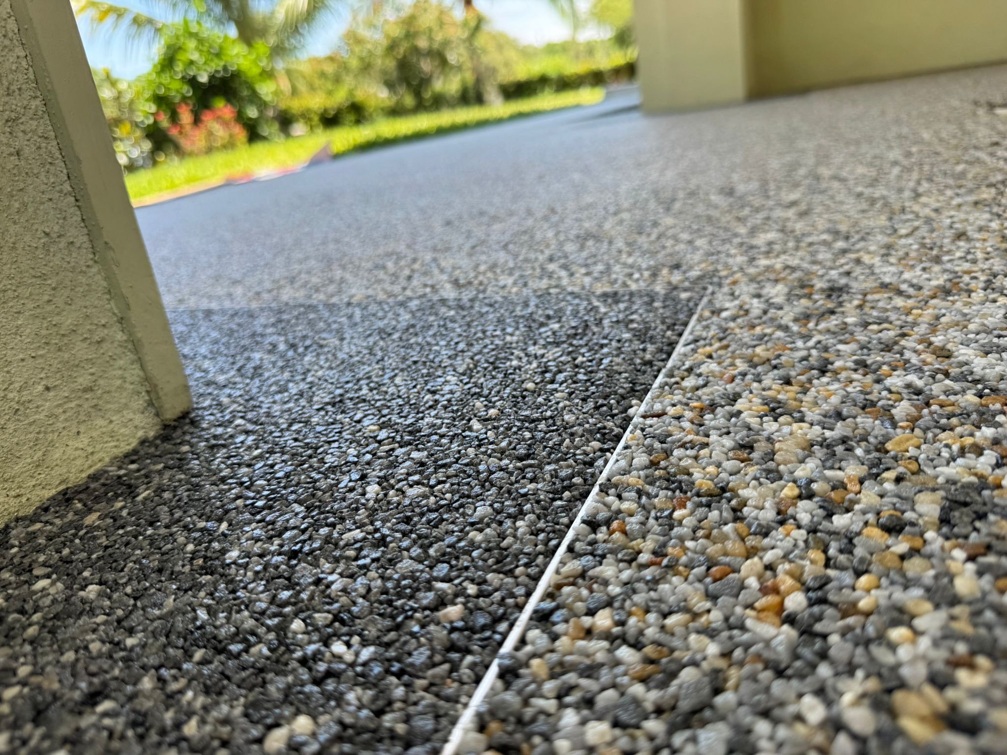 Close-up of textured outdoor flooring with a groove separating two sections, with a grassy area and trees in the background.