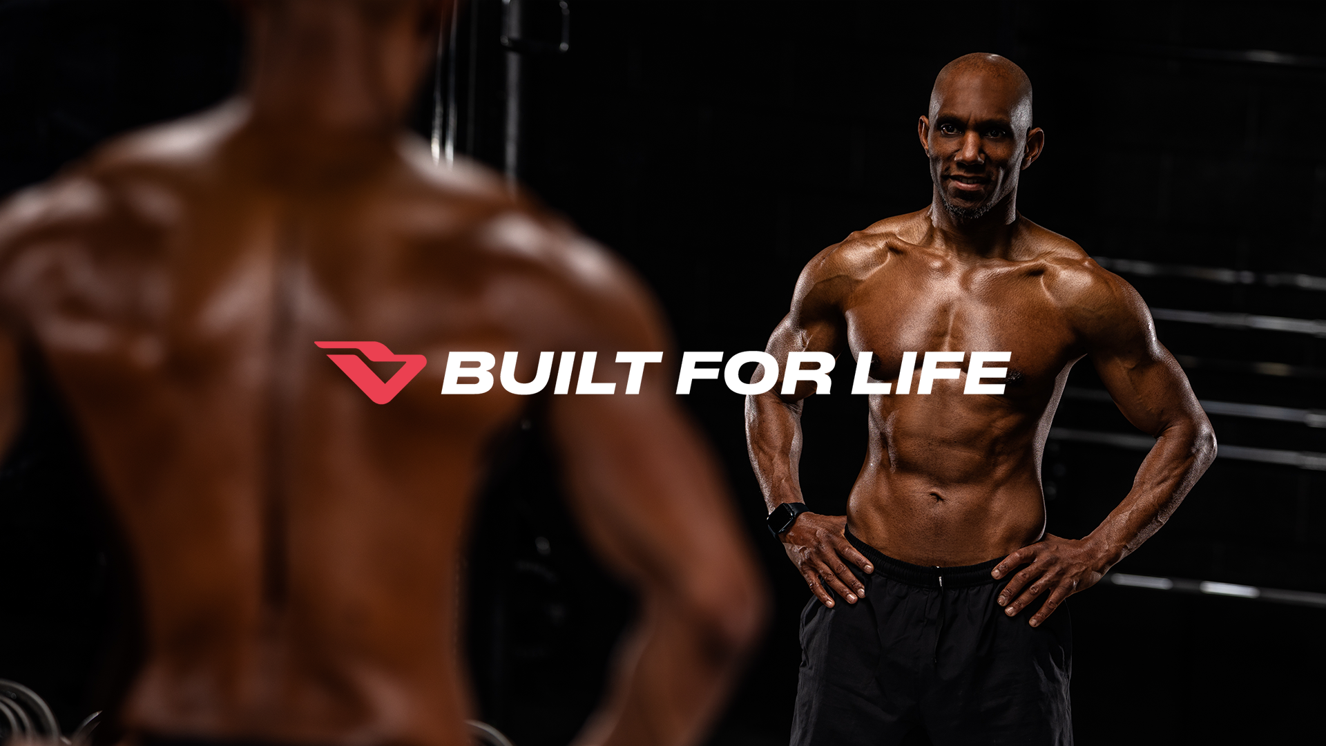 Two shirtless men with muscular physiques in a gym, one in the foreground and one in the background, with the slogan 'Built for Life' and a logo overlay.