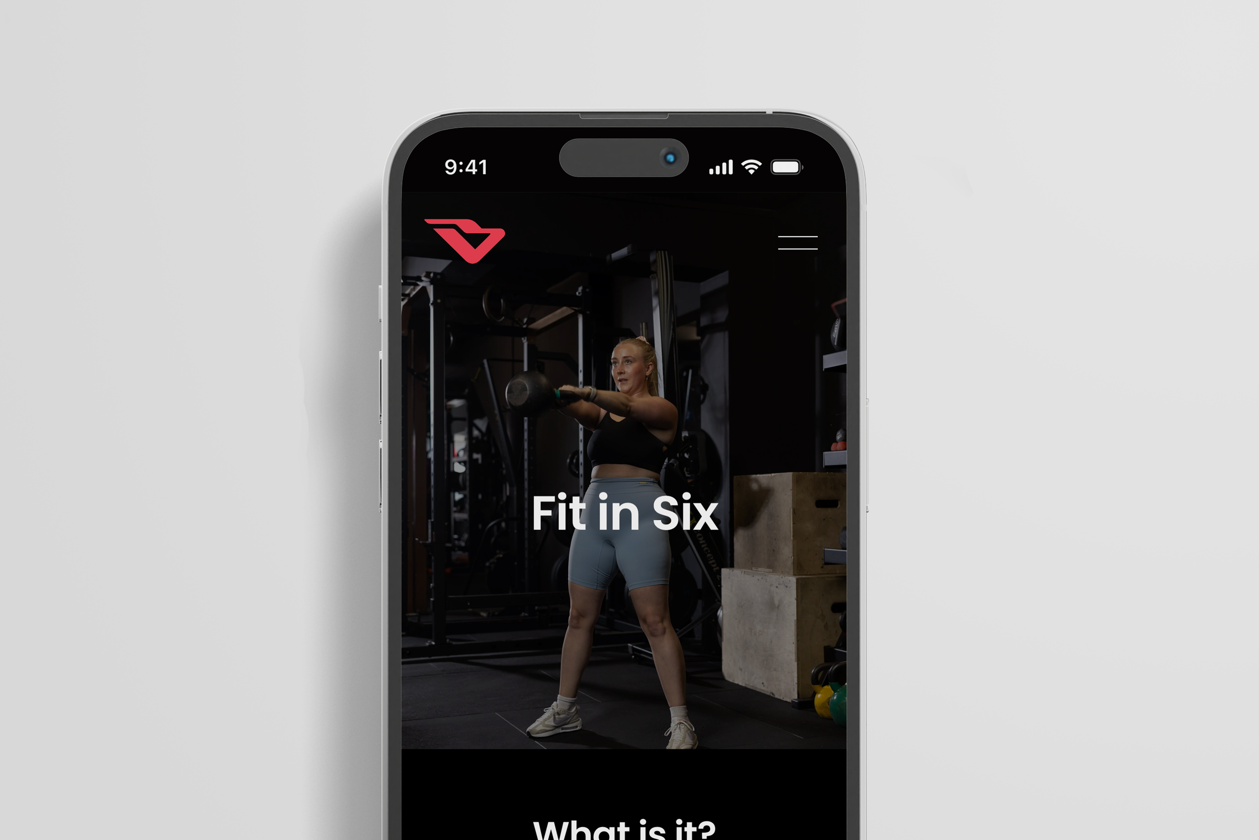 Smartphone displaying a fitness app called 'Fit in Six' with a woman lifting a kettlebell in a gym.