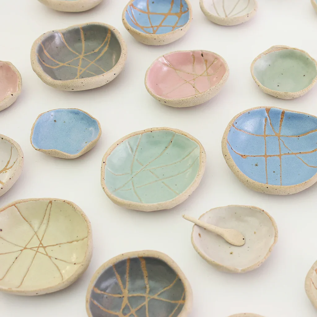 Small ceramic bowls with pastel-colored glazes and gold crackle patterns, some with matching spoons, arranged on a white surface.