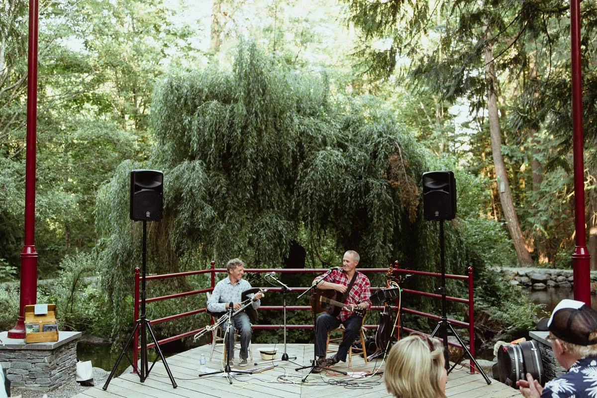 Two musicians playing guitars on an outdoor stage in a lush, wooded park. One is Terry Boyle, Irish folk singer and guitar player, and the other is Martin Nolan, Irish uilleann pipe player.