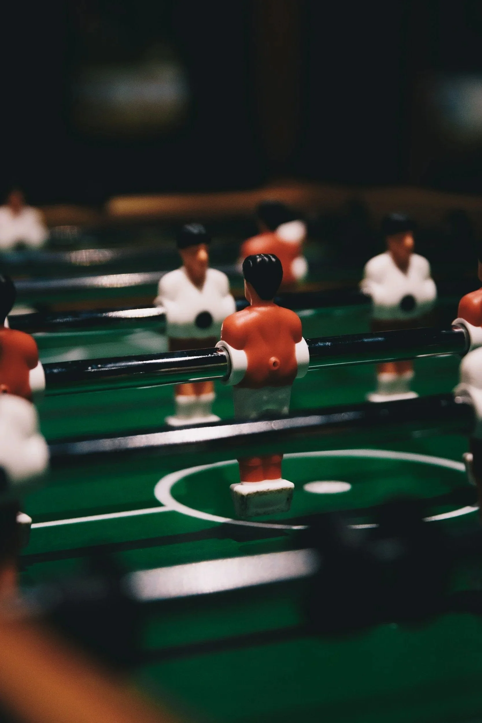 Close-up of a foosball table with plastic players, some painted with tan skin and black hair, on a green playing field.