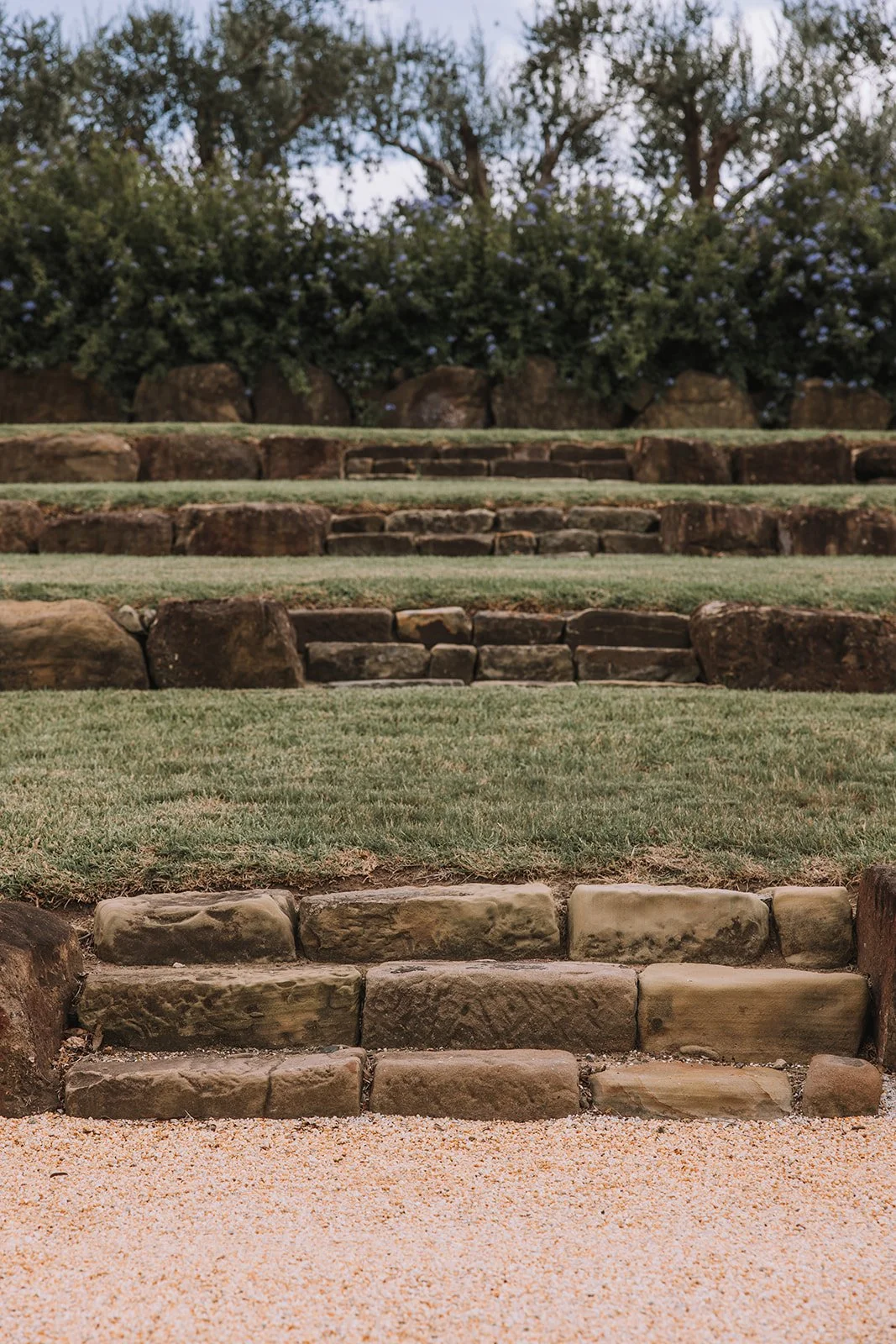 Stone steps leading up a grassy hill with bushes and trees in the background.