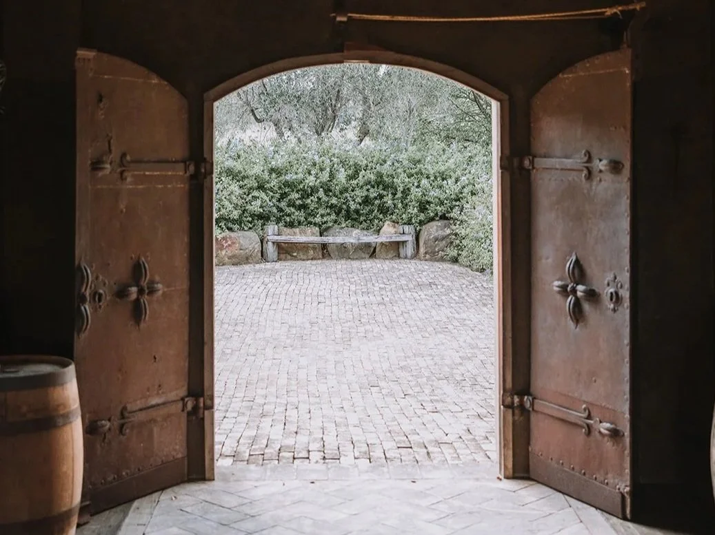Open wooden doors leading to a small courtyard with a bush and a stone bench.