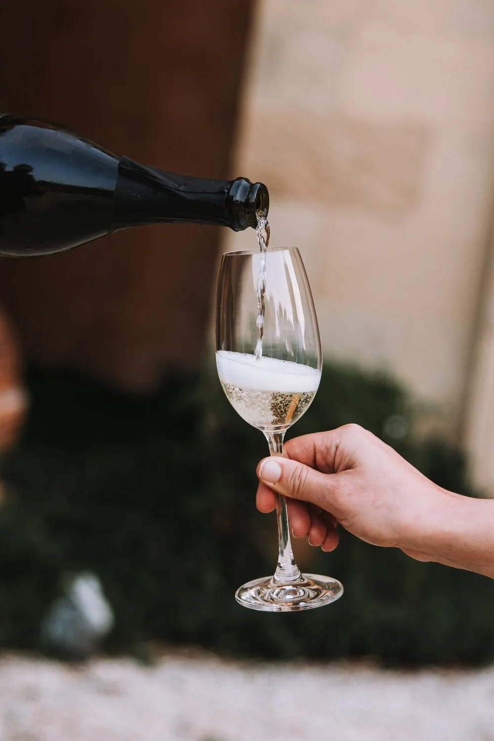 A person is pouring champagne into a wine glass. The background is blurred.