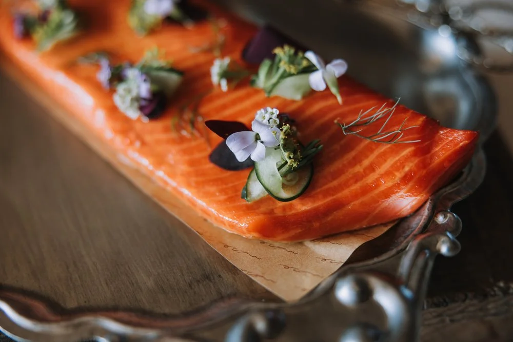 Salmon fillet garnished with edible flowers and herbs on a decorative silver tray.