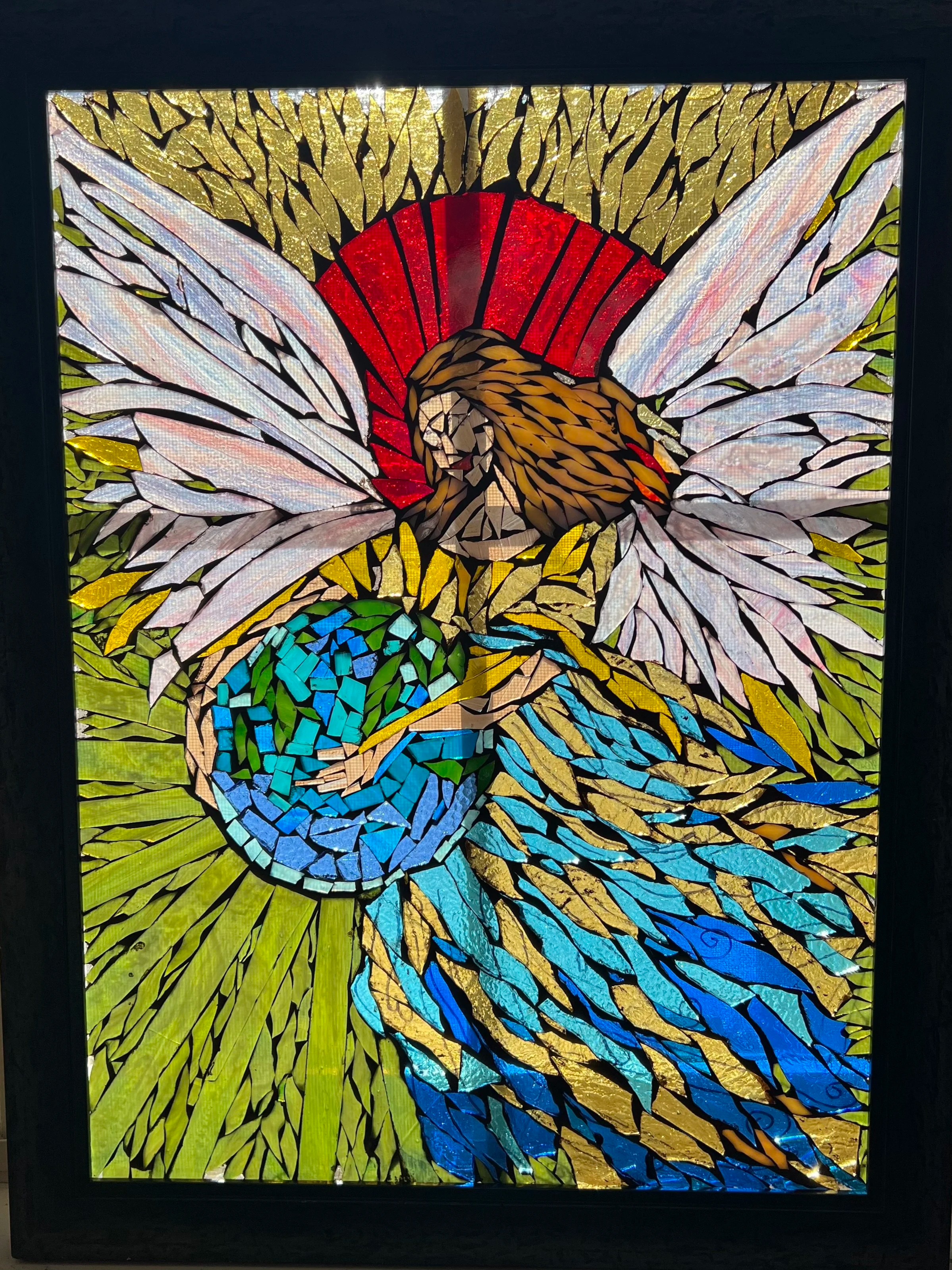 Karen Whalen Original Art | Lake Geneva Art Studio | Stained glass artwork of an angel with outstretched wings, holding the earth, with a red circular halo, surrounded by green foliage.