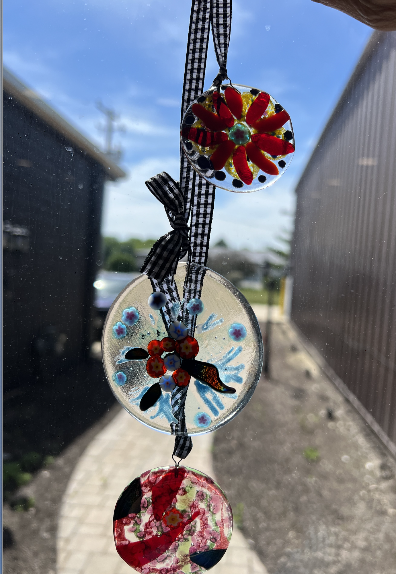 Colorful glass wind chimes hanging outdoors with a blue sky and buildings in the background.