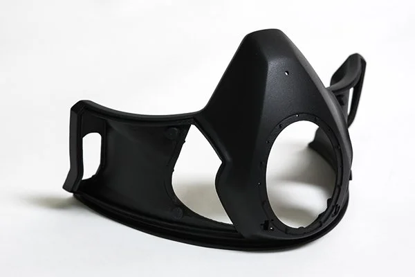 A black oxygen mask with a clear plastic tube attached, placed on a white surface.