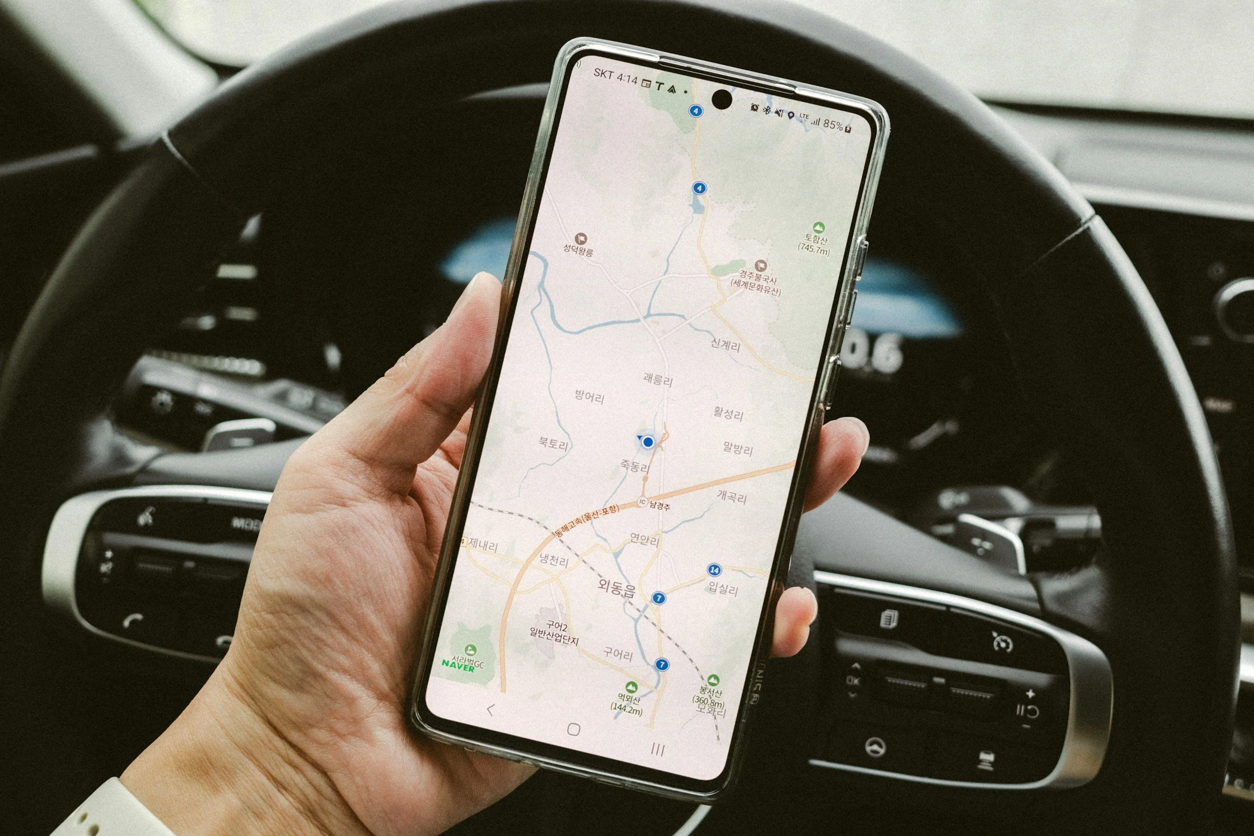 A person holding a smartphone displaying a map while sitting in the driver's seat of a car.