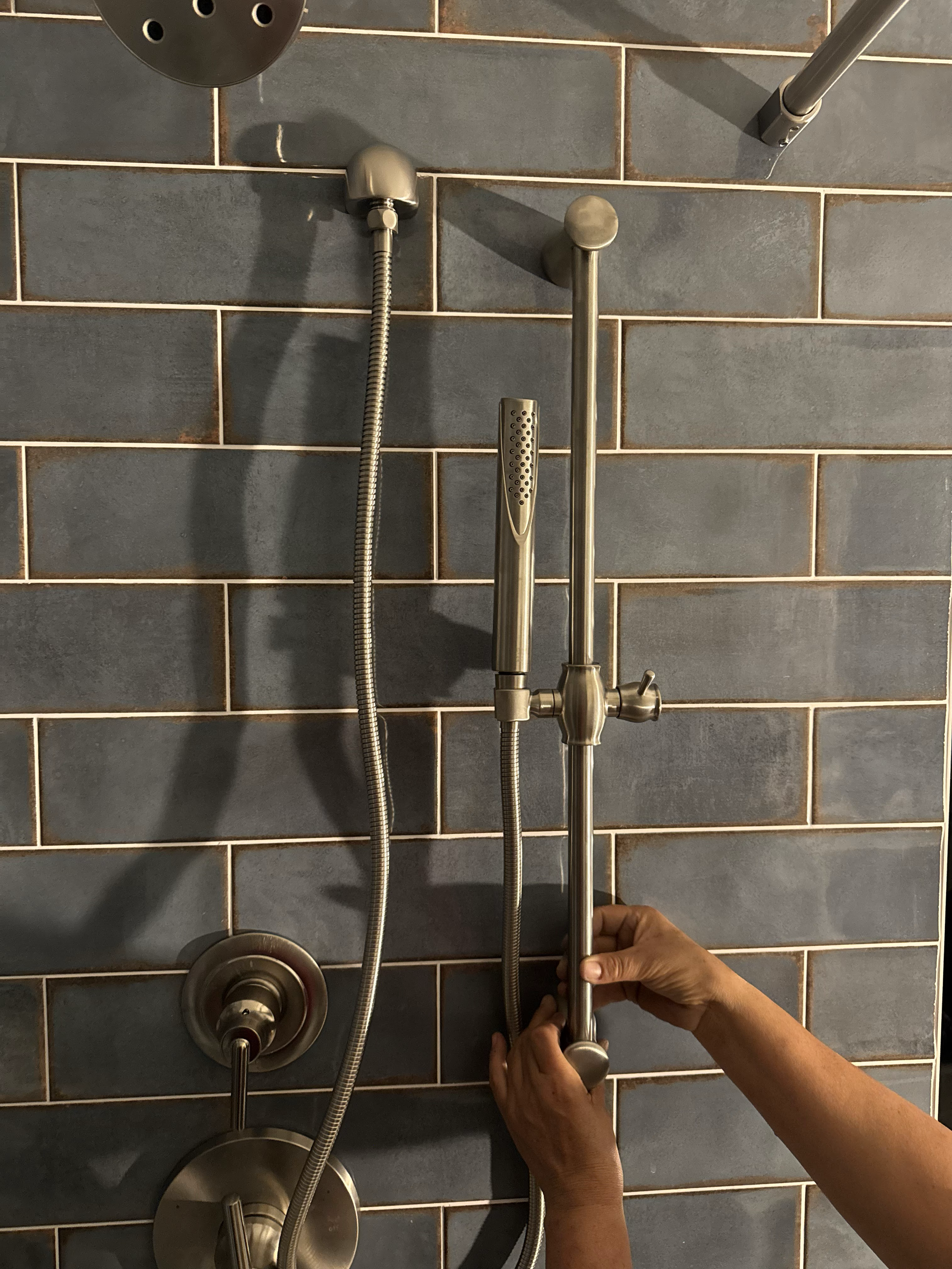 A person adjusting a shower handle in a bathroom with gray tiled walls.