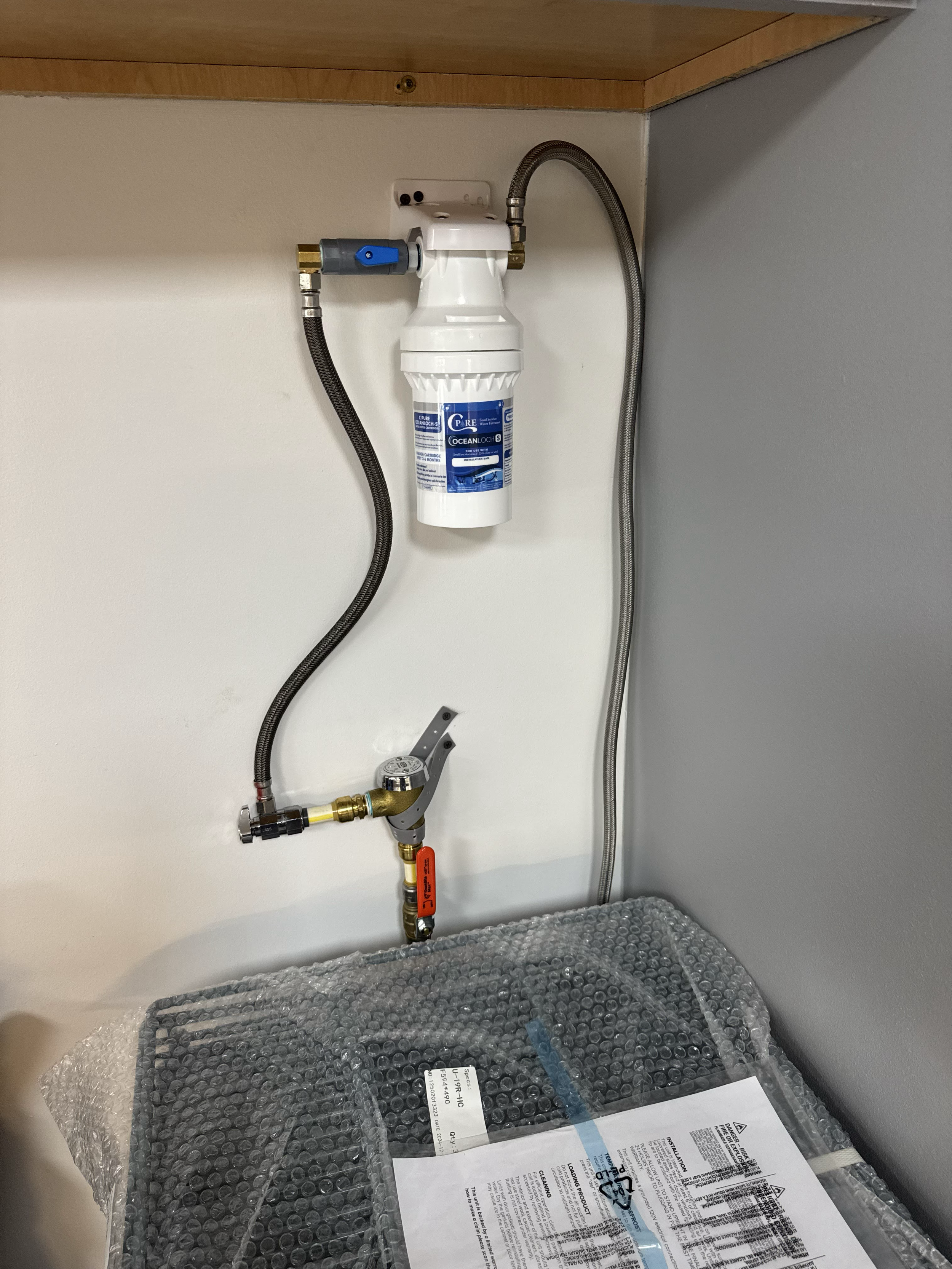 Water filtration system installed under the sink with associated hoses and a wrapped water filter