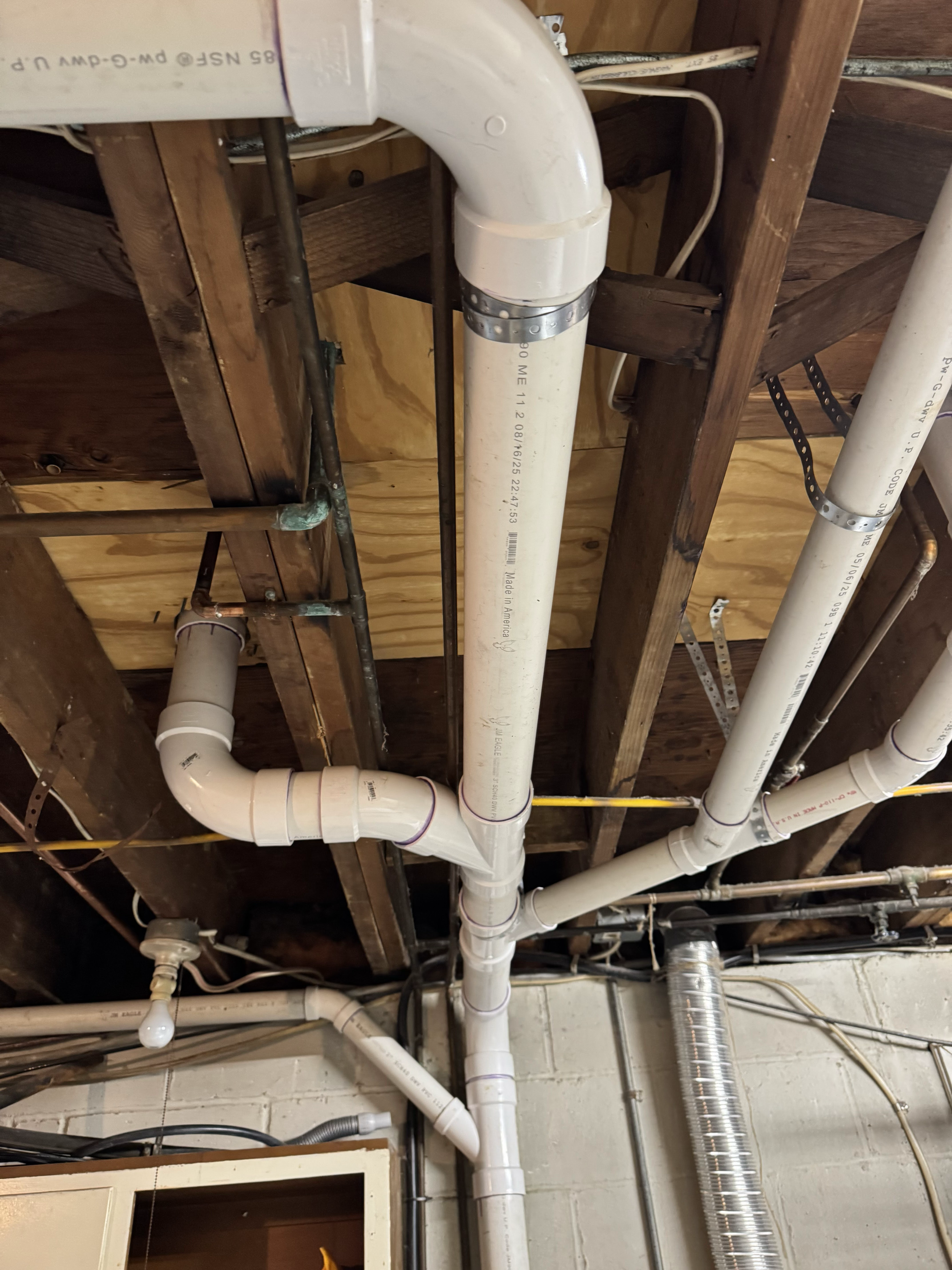 View of plumbing pipes running along a wooden ceiling with metal brackets and screws.