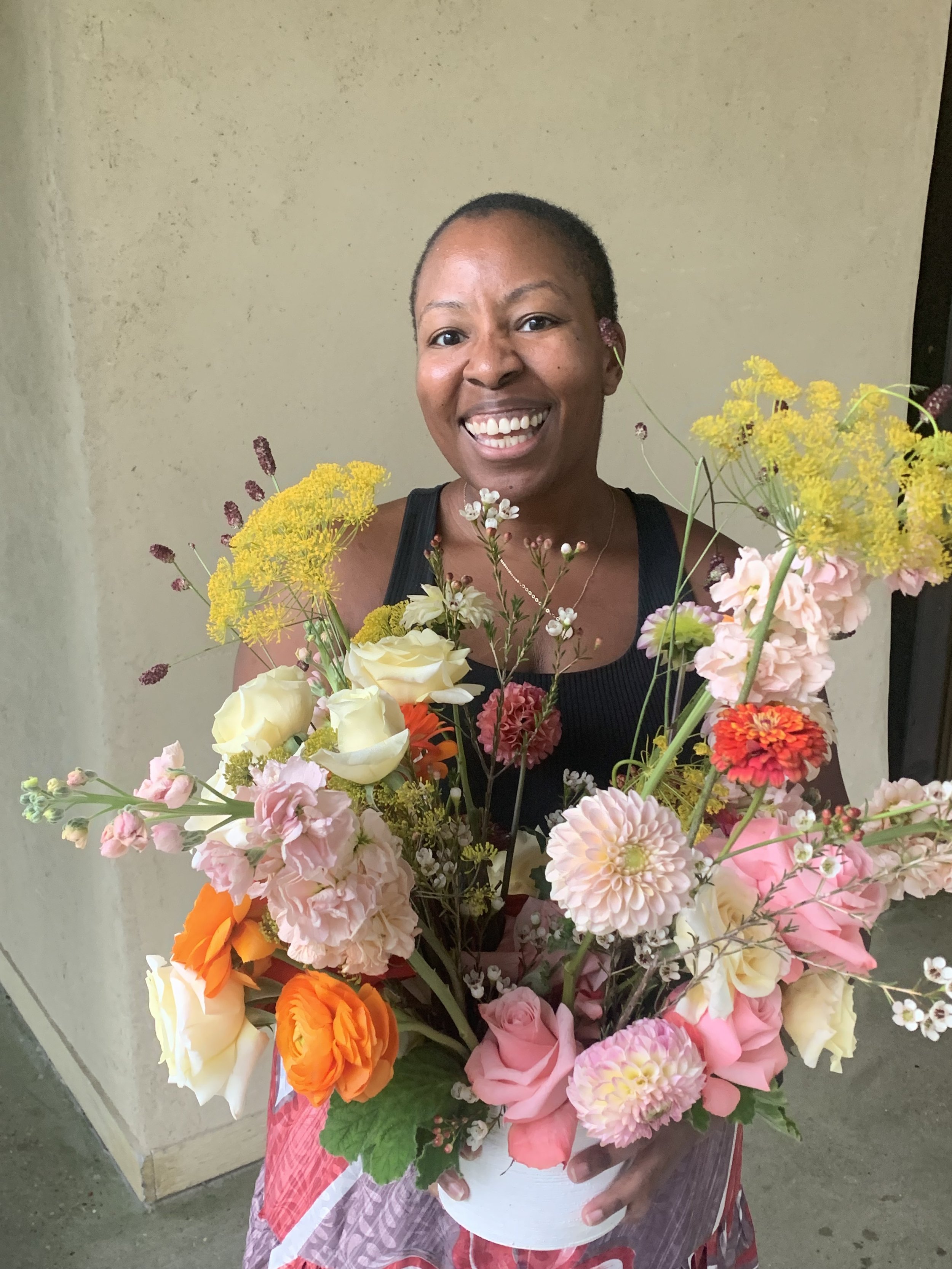 A woman holding a large bouquet of colorful flowers including roses, carnations, and daisies, while smiling at the camera.