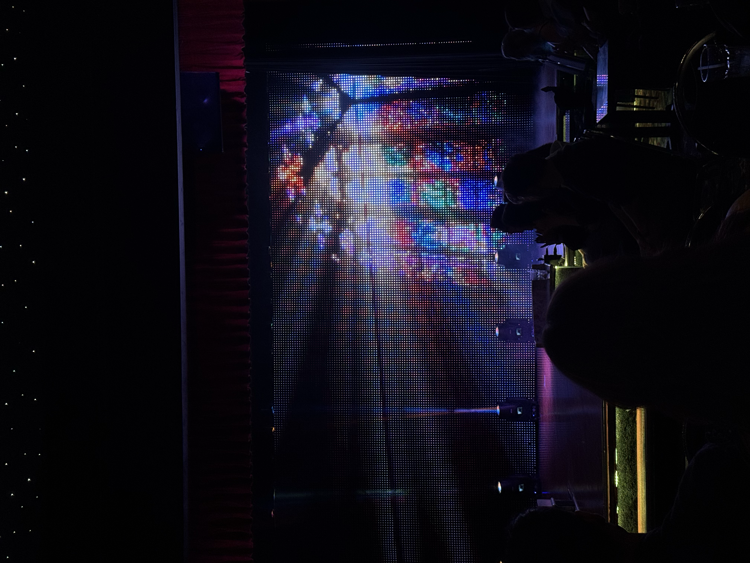 Audience watching a colorful digital fireworks display on a large screen in a dark indoor setting.