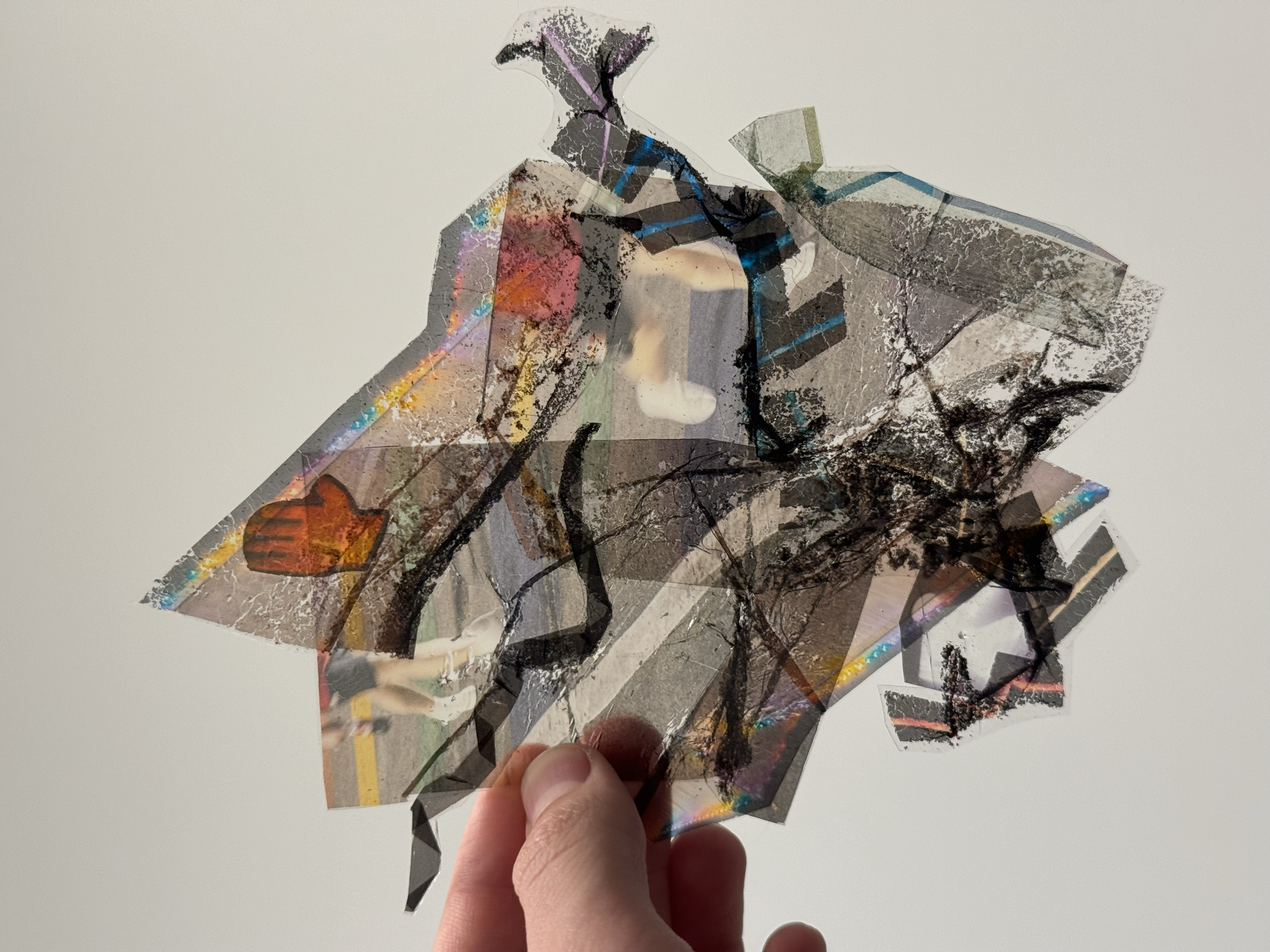 A hand holding multiple overlapping pieces of transparent, reflective, and damaged plastic with graffiti and street art.