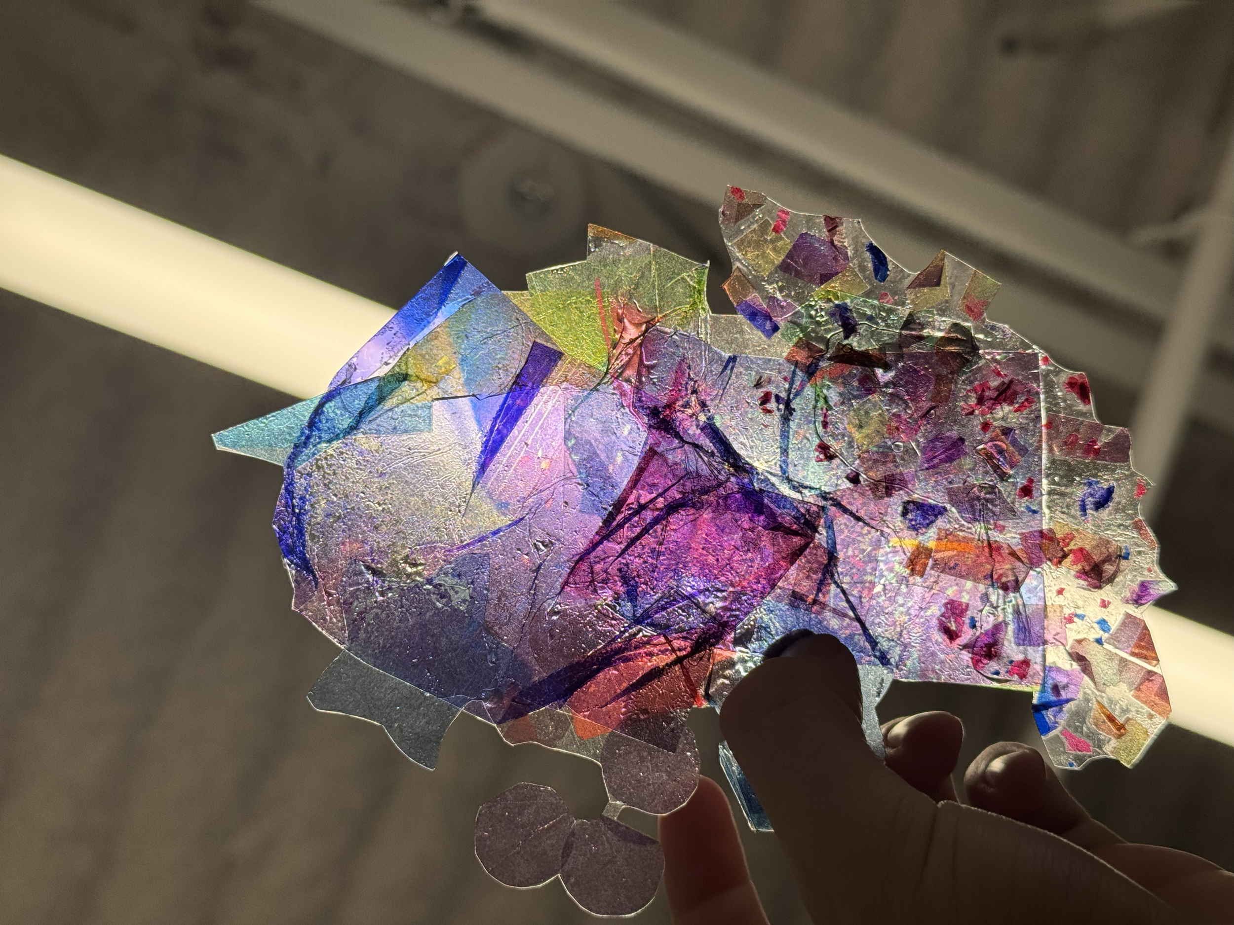 A colorful, abstract, crumpled piece of translucent paper or plastic held up against light, displaying various colors and textures.