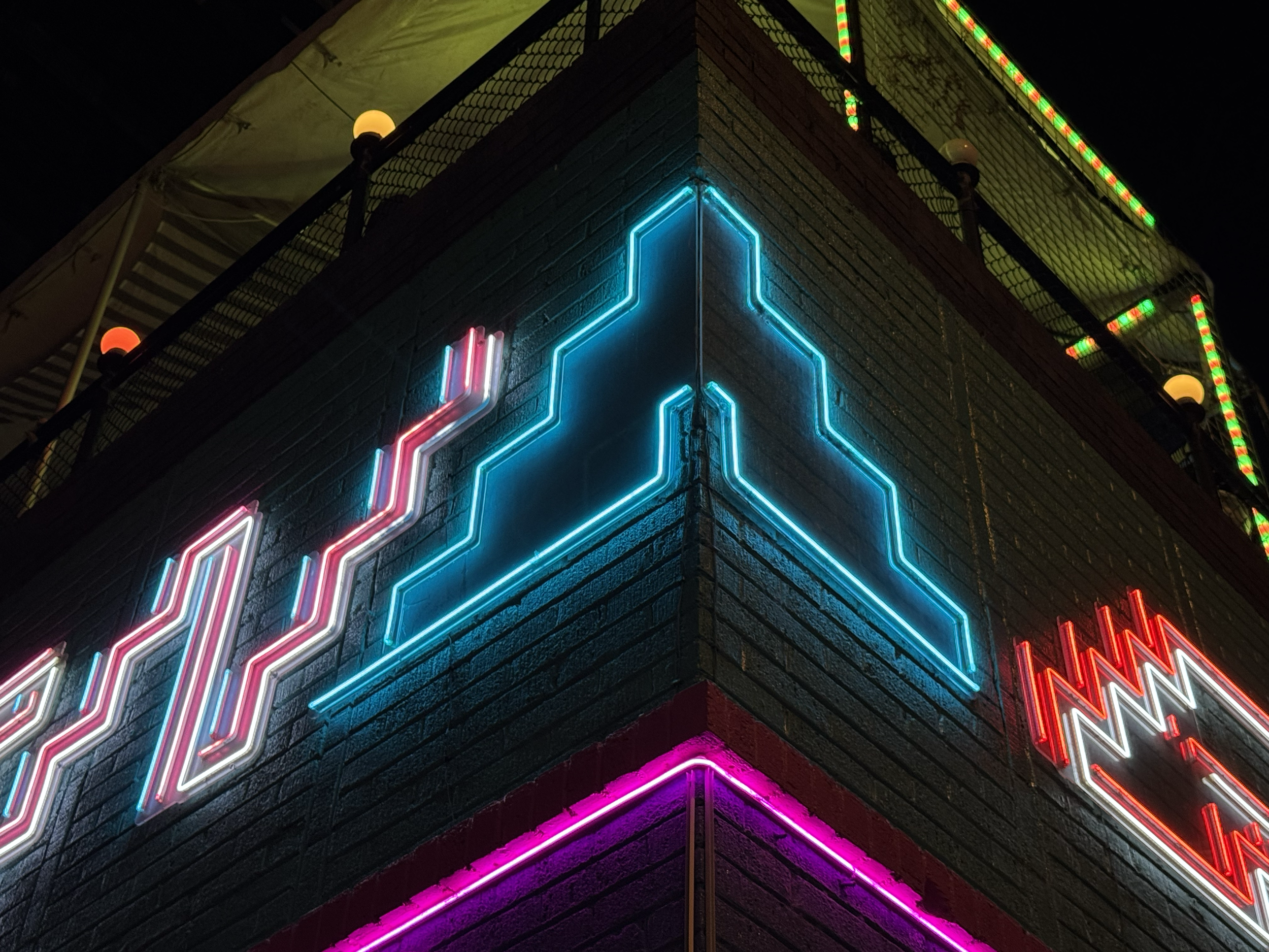 Colorful neon lights forming geometric patterns on a brick building at night with a balcony on top.