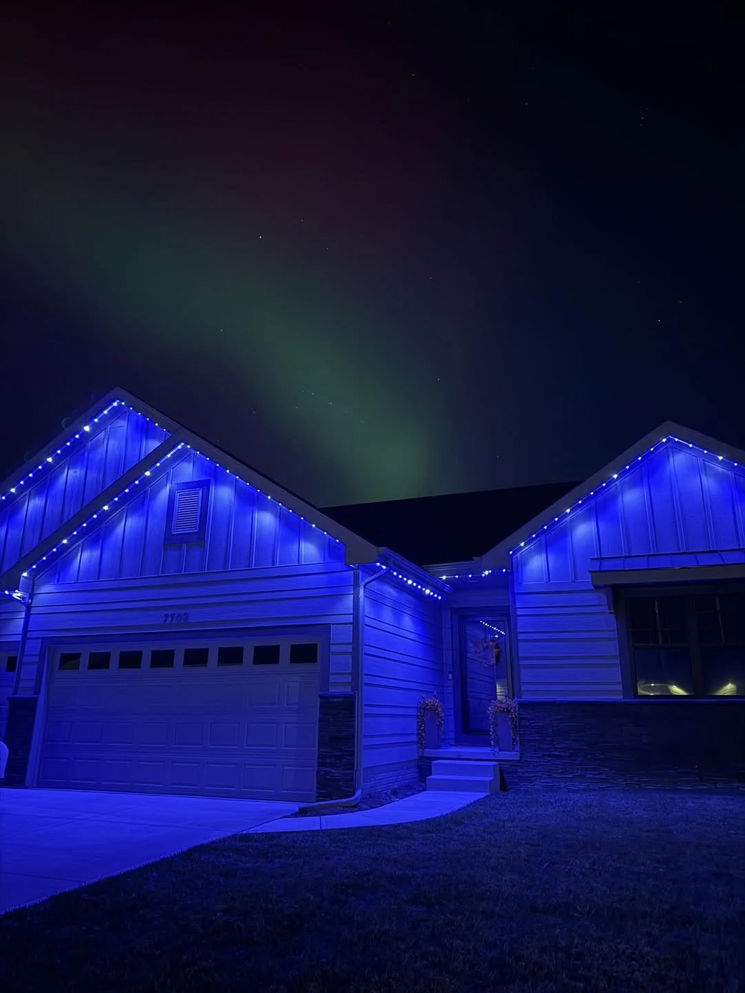 A house at night decorated with blue Christmas lights outlining the roof and garage, with a dark sky above.