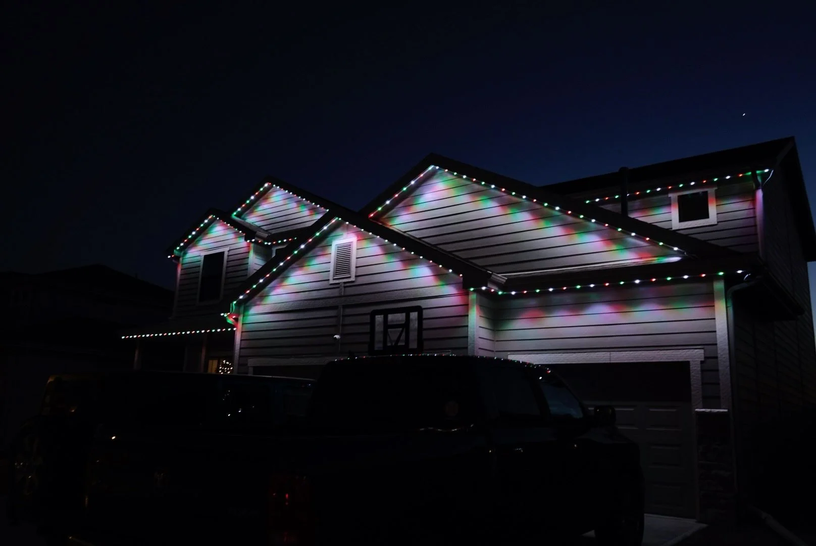 A house decorated with colorful Christmas lights at night, with a dark sky overhead.