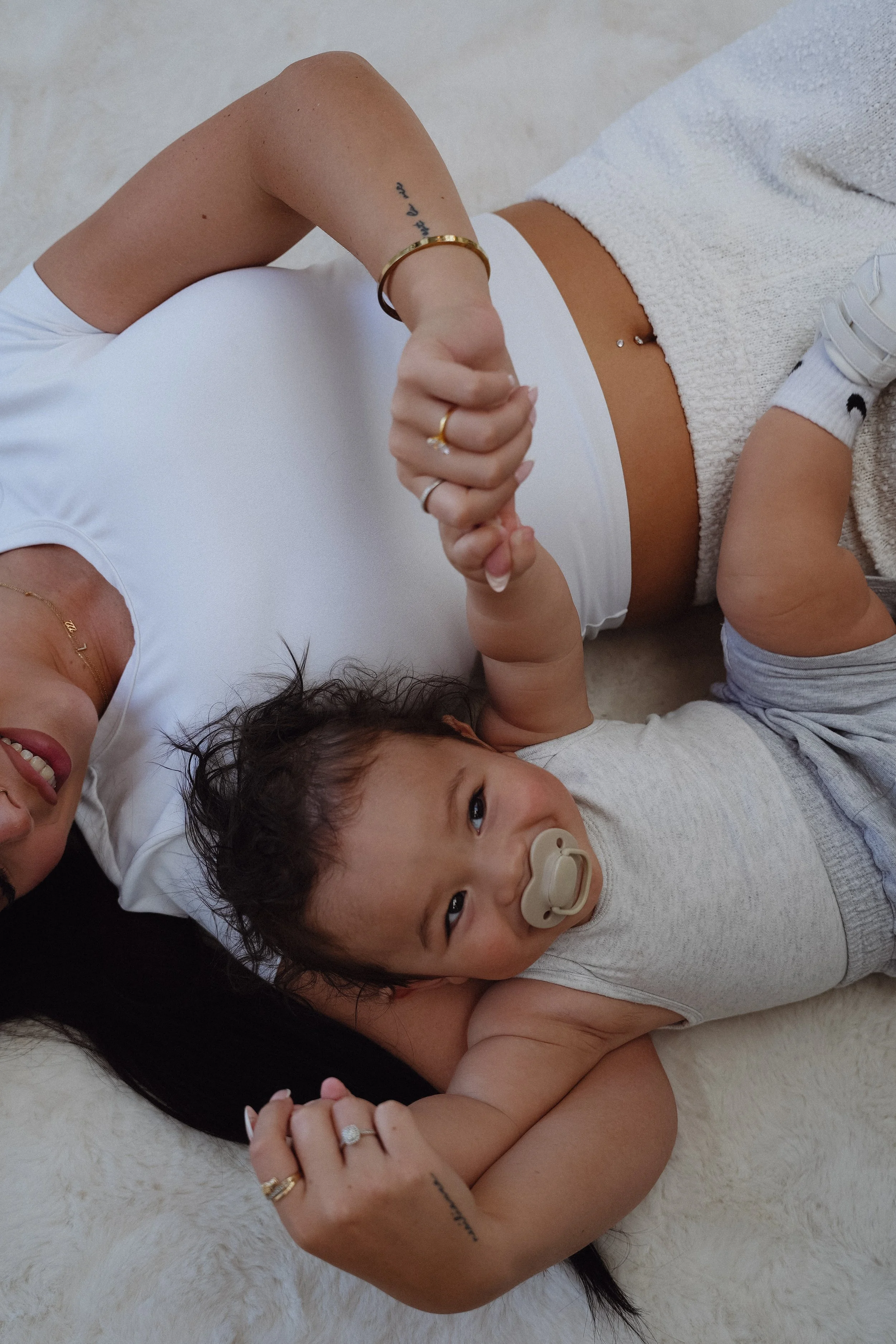 A woman and a young child lying on a soft surface, holding hands, with the child using a pacifier.