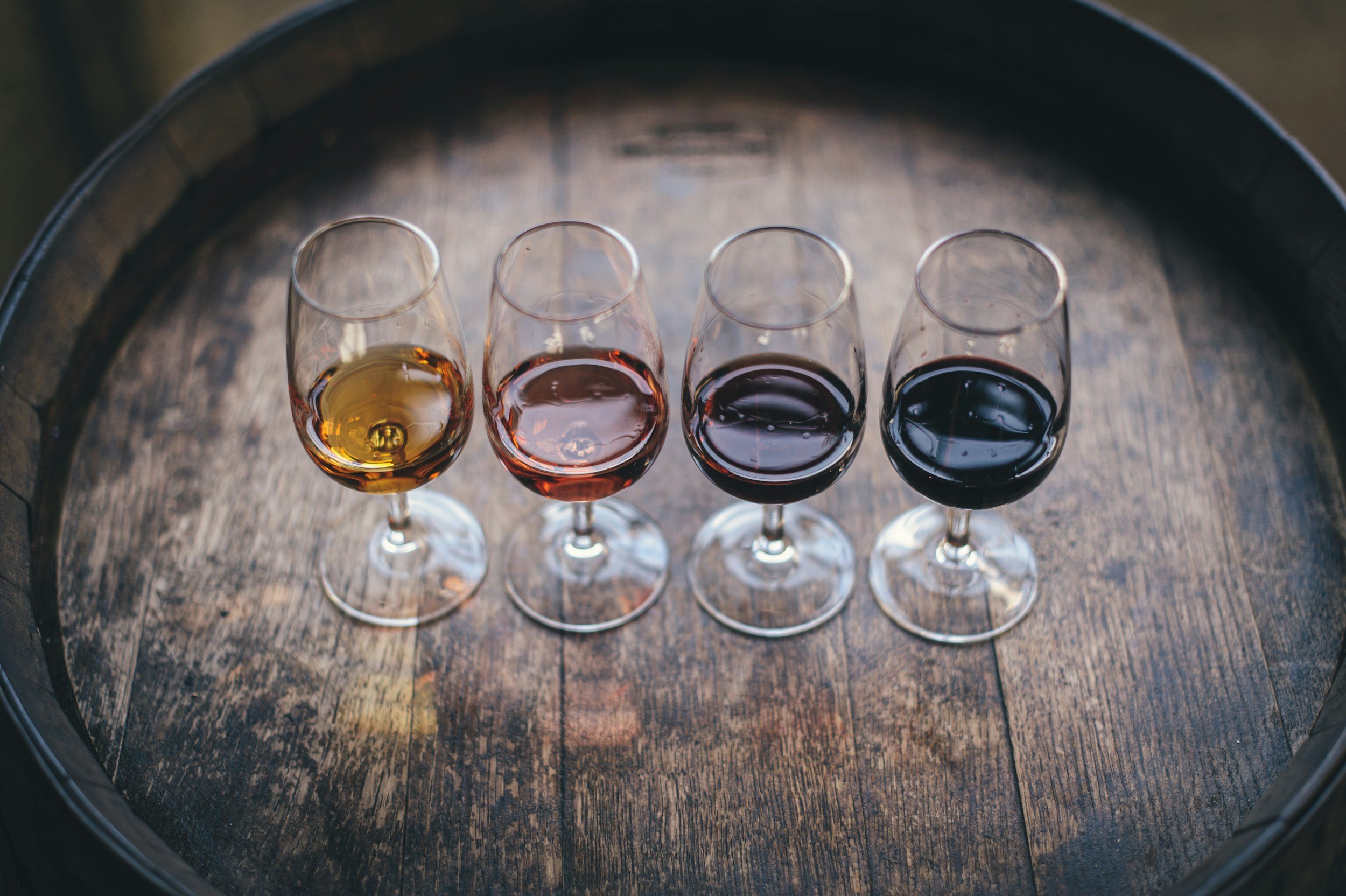 Four wine glasses filled with different types of wine, placed on a wooden surface inside a barrel.