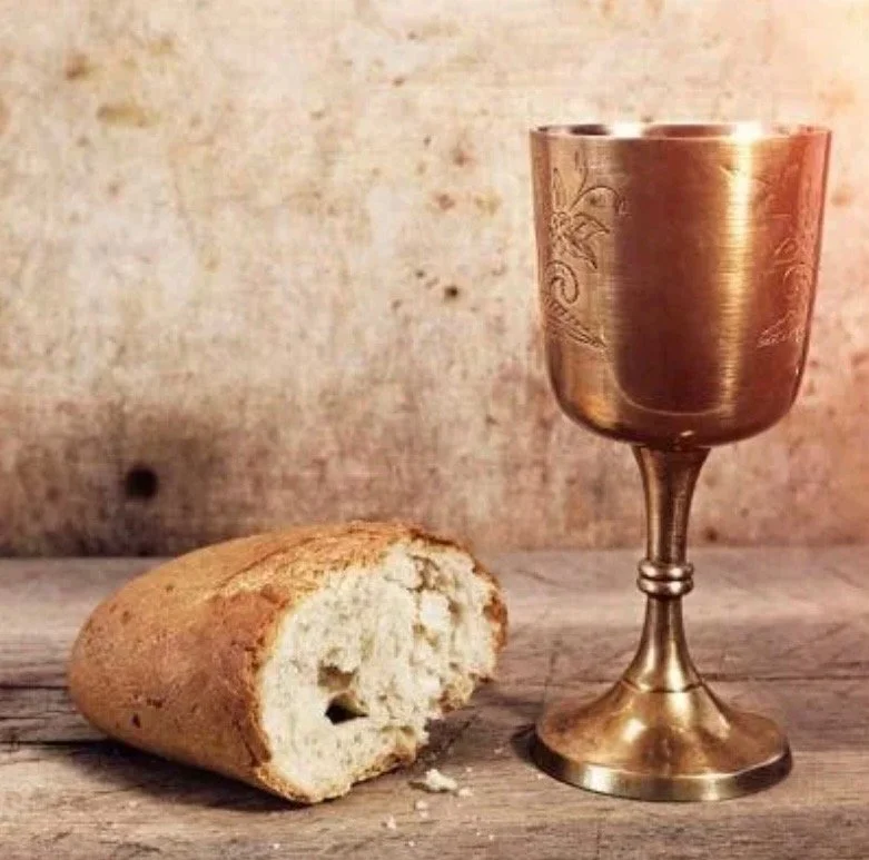 A bread roll with a bite taken out, and a metallic goblet on a wooden surface with a rustic background.