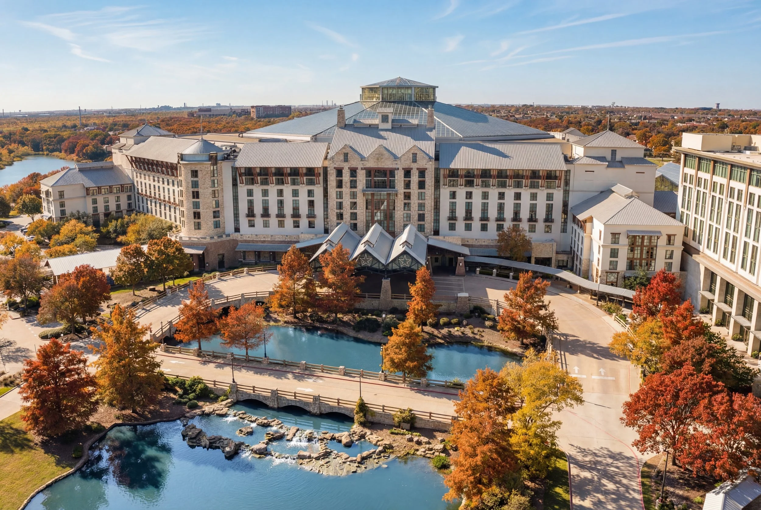 Aerial view of a large hotel with a courtyard, landscaped with colorful trees and water features, during fall.