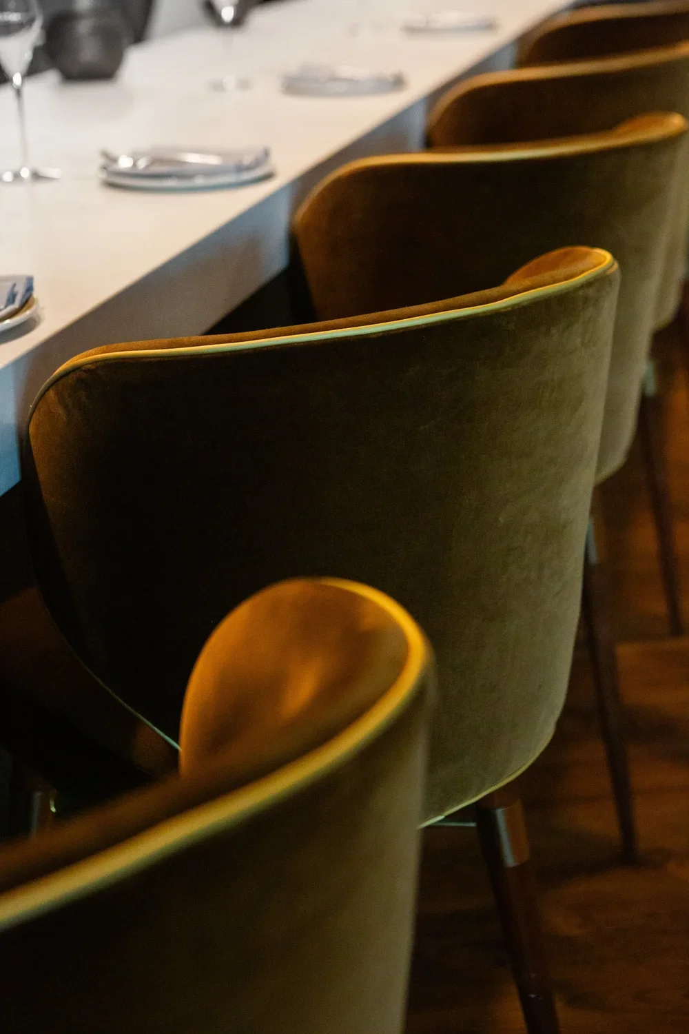 Close-up of green velvet chairs with wooden legs around a restaurant table with cutlery and napkins.