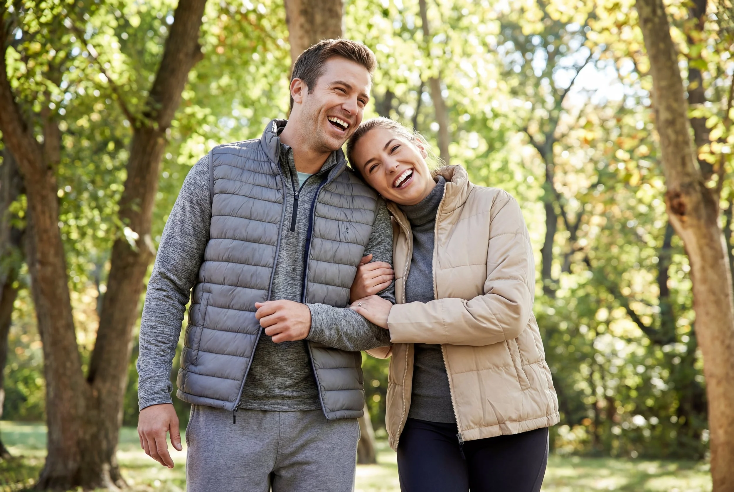 A smiling couple outdoors in a park during daytime, embracing each other.