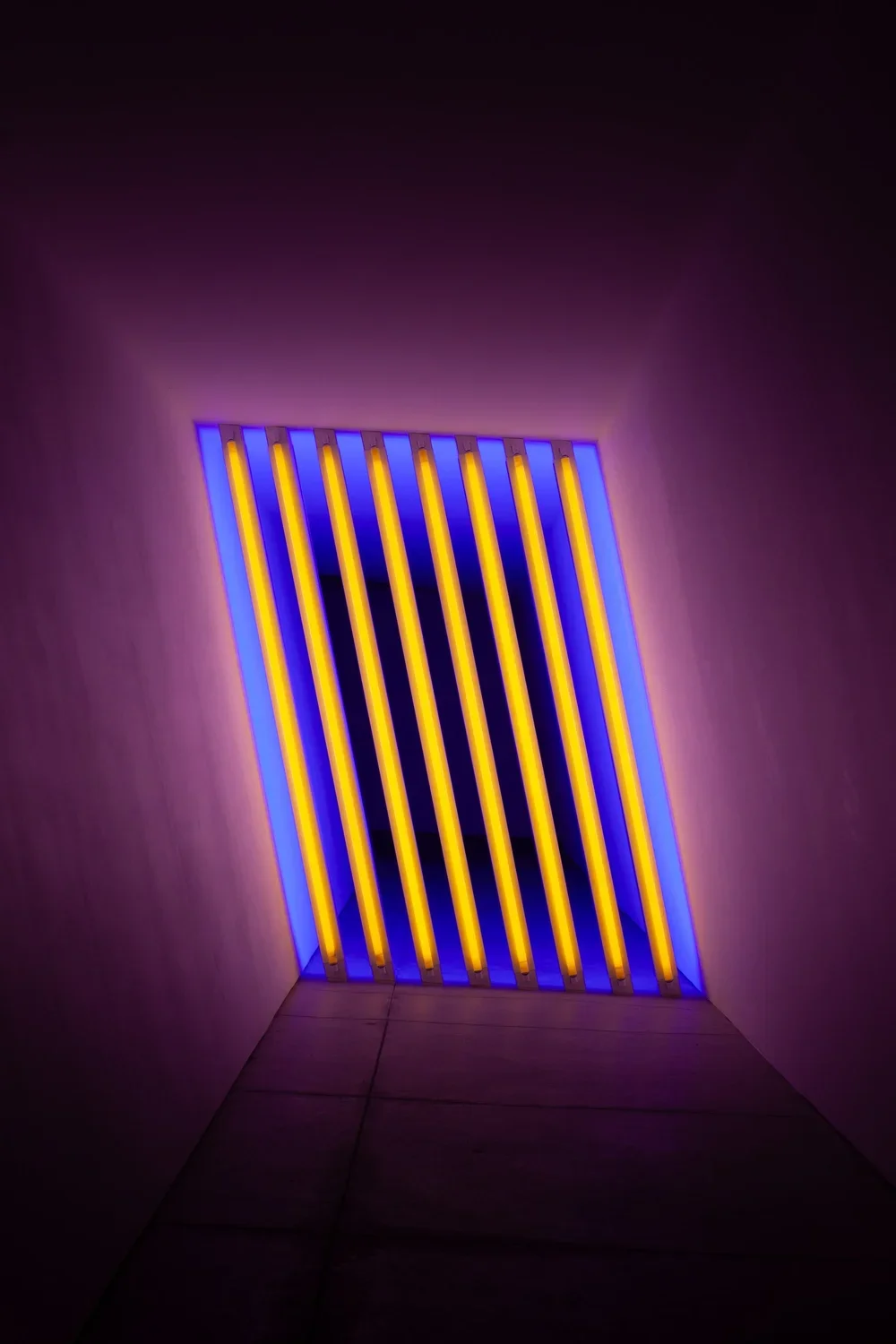 A tunnel with neon yellow and blue striped lighting on the ceiling, creating a vibrant glow against the surrounding walls.