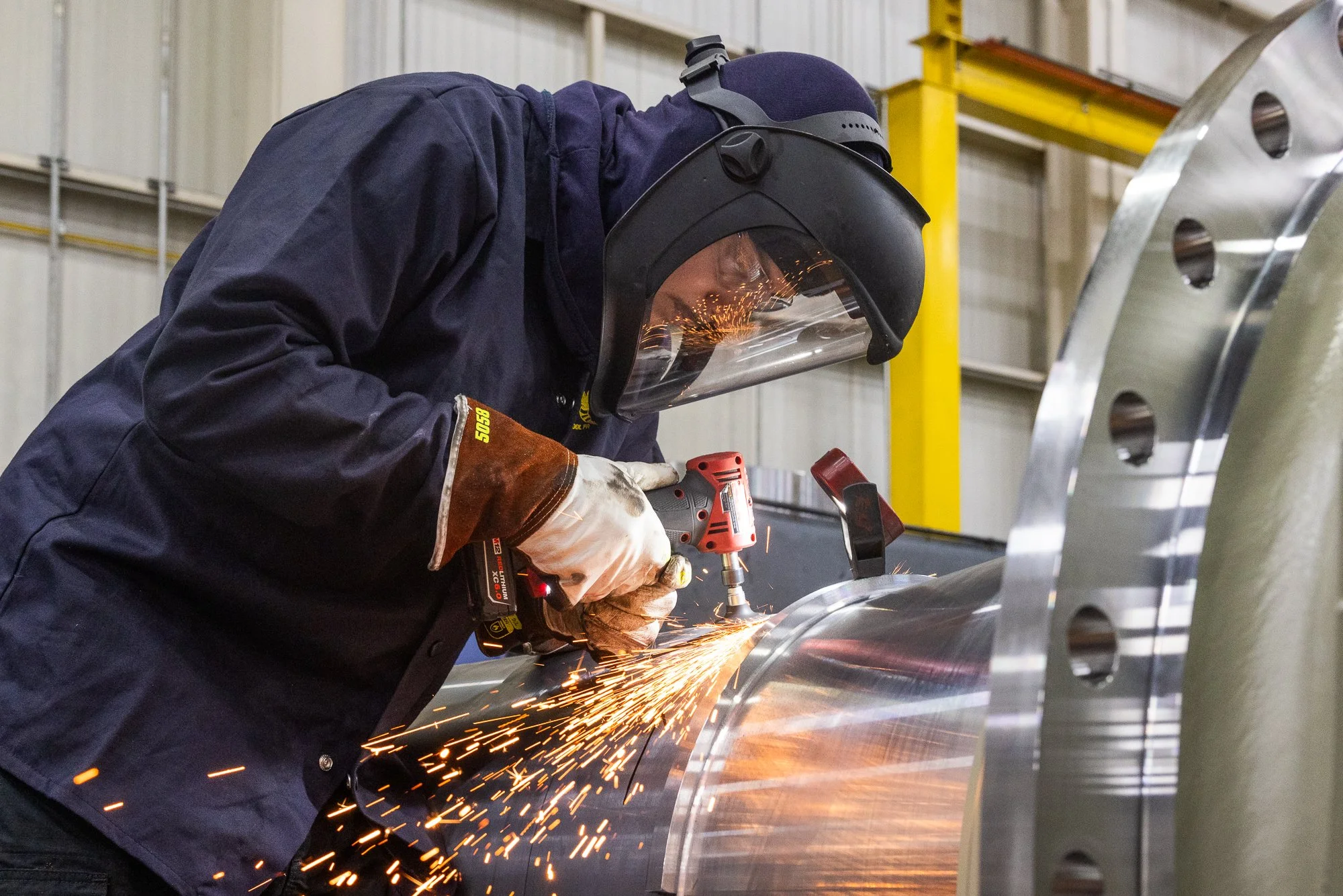 A welder working on a metal pipe, wearing protective gear and sparks flying.
