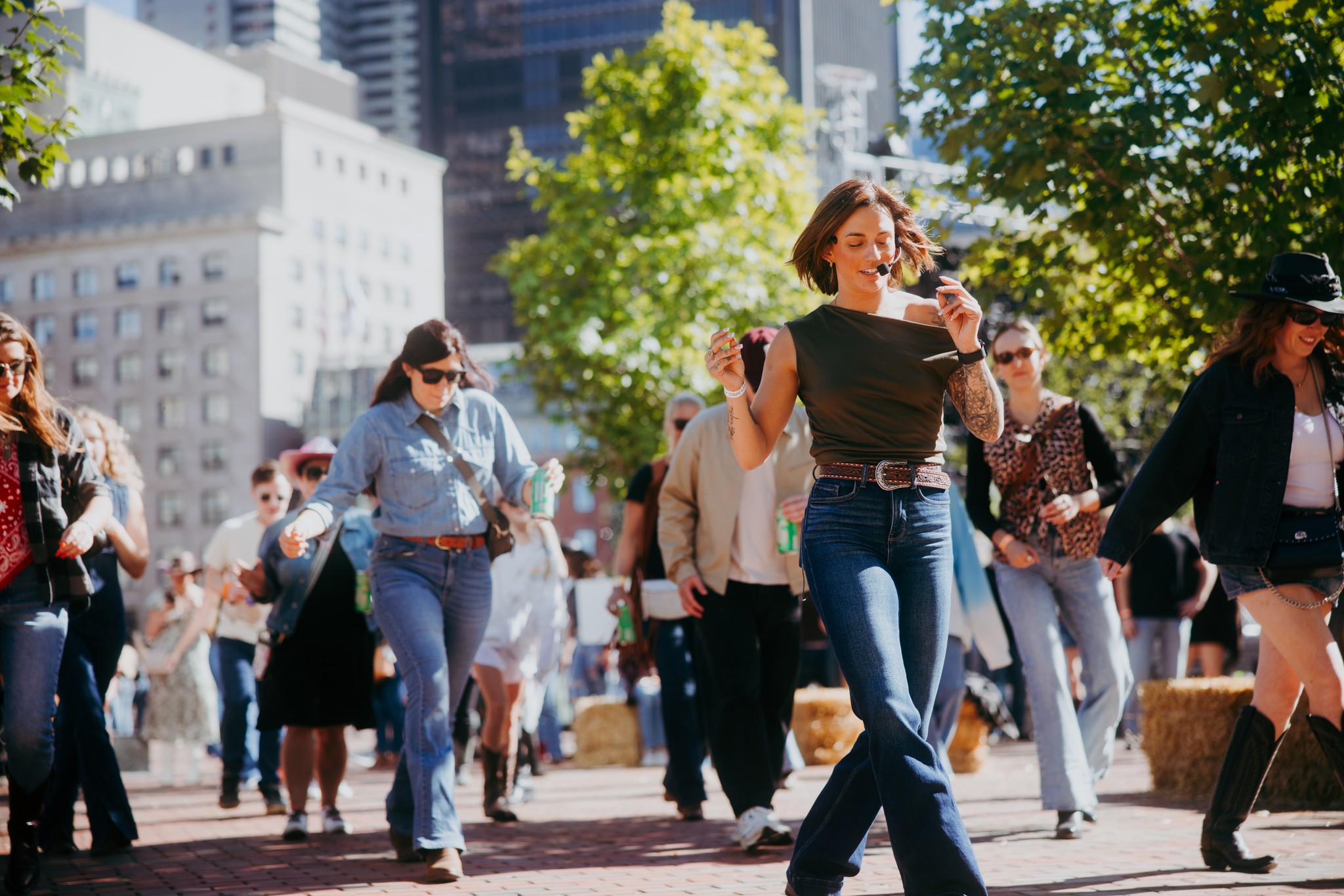 A woman with long blonde hair wearing a large white cowboy hat walking outdoors near a wooden fence with trees in the background, captured with a motion blur effect.