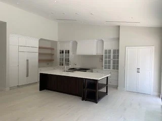 Empty modern kitchen with white cabinets, a dark island, and light-colored flooring.