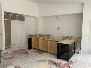 Empty kitchen with beige cabinets, white walls, and pink and gray flooring in a room under renovation.