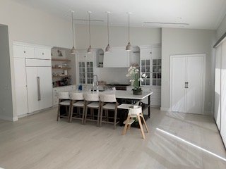 Modern white kitchen with an island, dining table, and chairs, with natural light coming from a window.