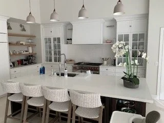 A modern white kitchen with a large island, white cabinets, and barstools.