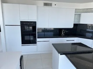 Modern kitchen with white cabinets, black countertops, and built-in appliances.