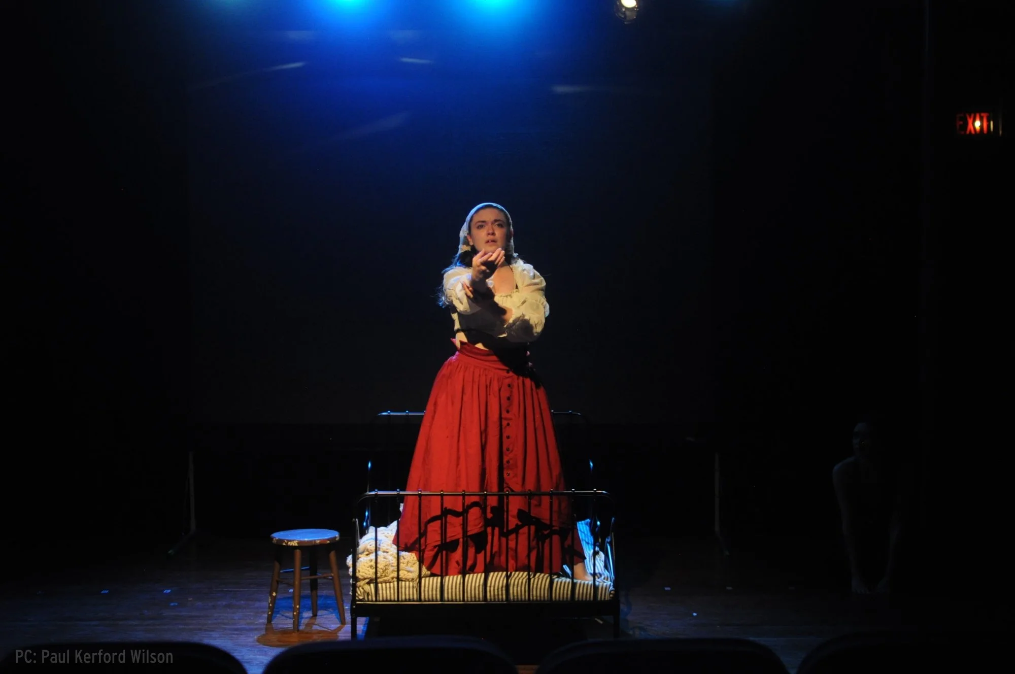 a white woman with dark hair in a red skirt stands on a bed reaching towards you
