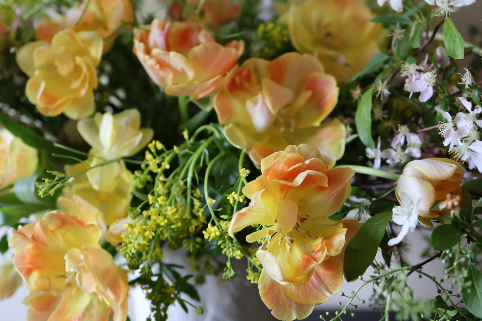Close-up of a mixed bouquet of yellow, peach, and pink flowers with green leaves.