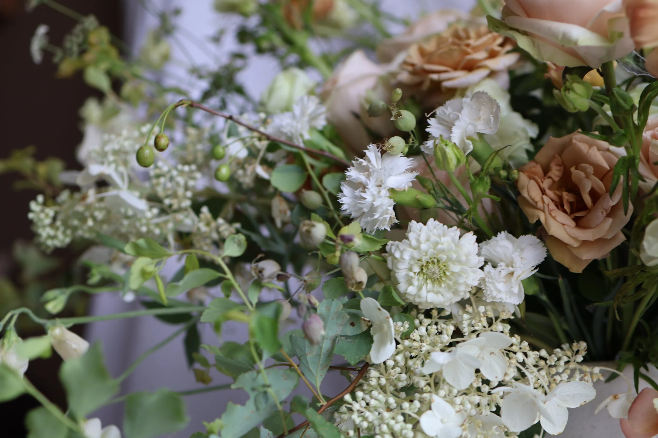 Close-up of a bouquet with white and peach-colored flowers, greenery, and small green buds.