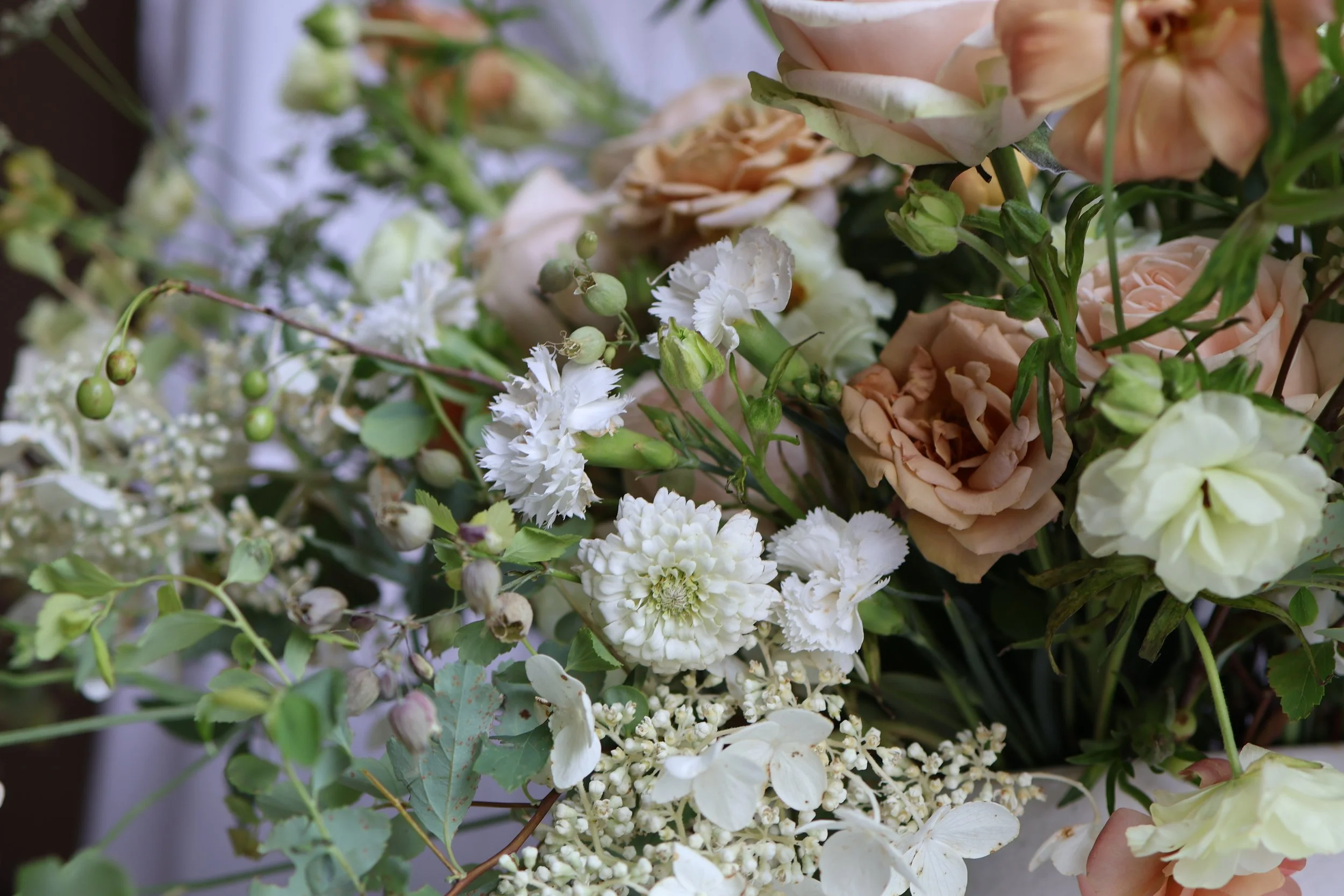 Close-up of a bouquet of pastel-colored roses and white flowers with green foliage.