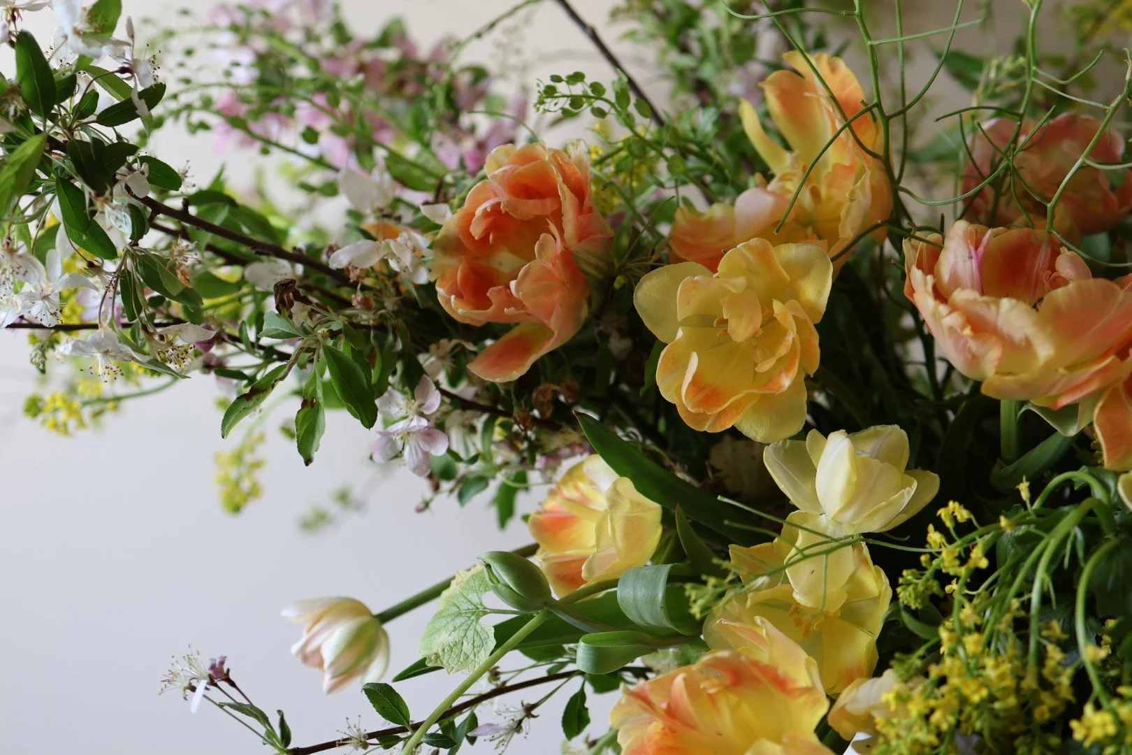 A lush floral arrangement with peach and yellow tulips, small white and pink flowers, and green leaves.